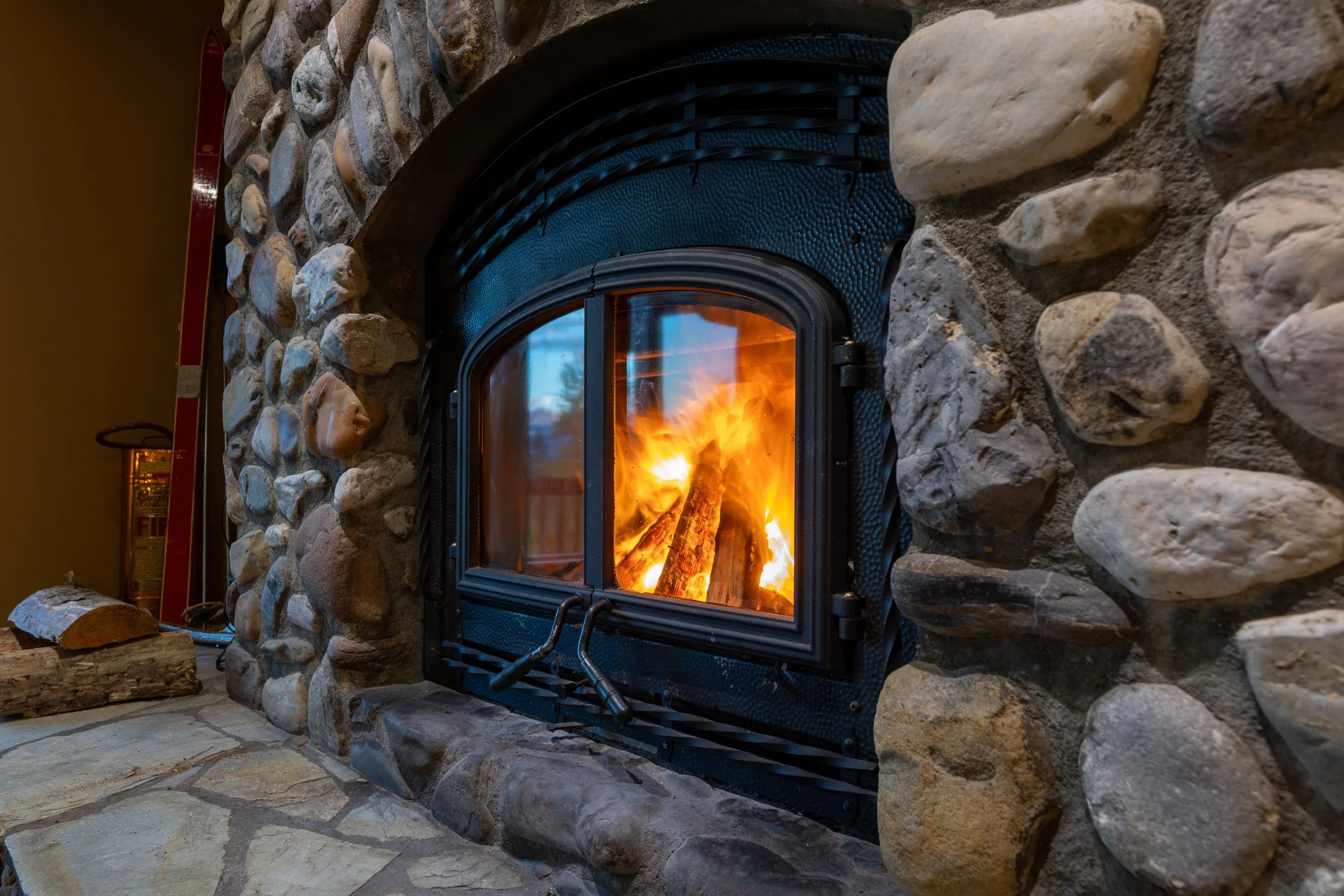 A cozy stone fireplace with a burning fire inside, surrounded by large rocks and a stone hearth.