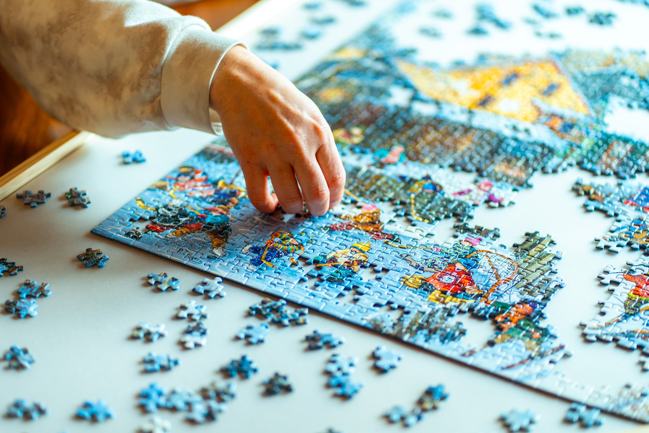 A person's hand arranging pieces of a colorful jigsaw puzzle on a white surface.