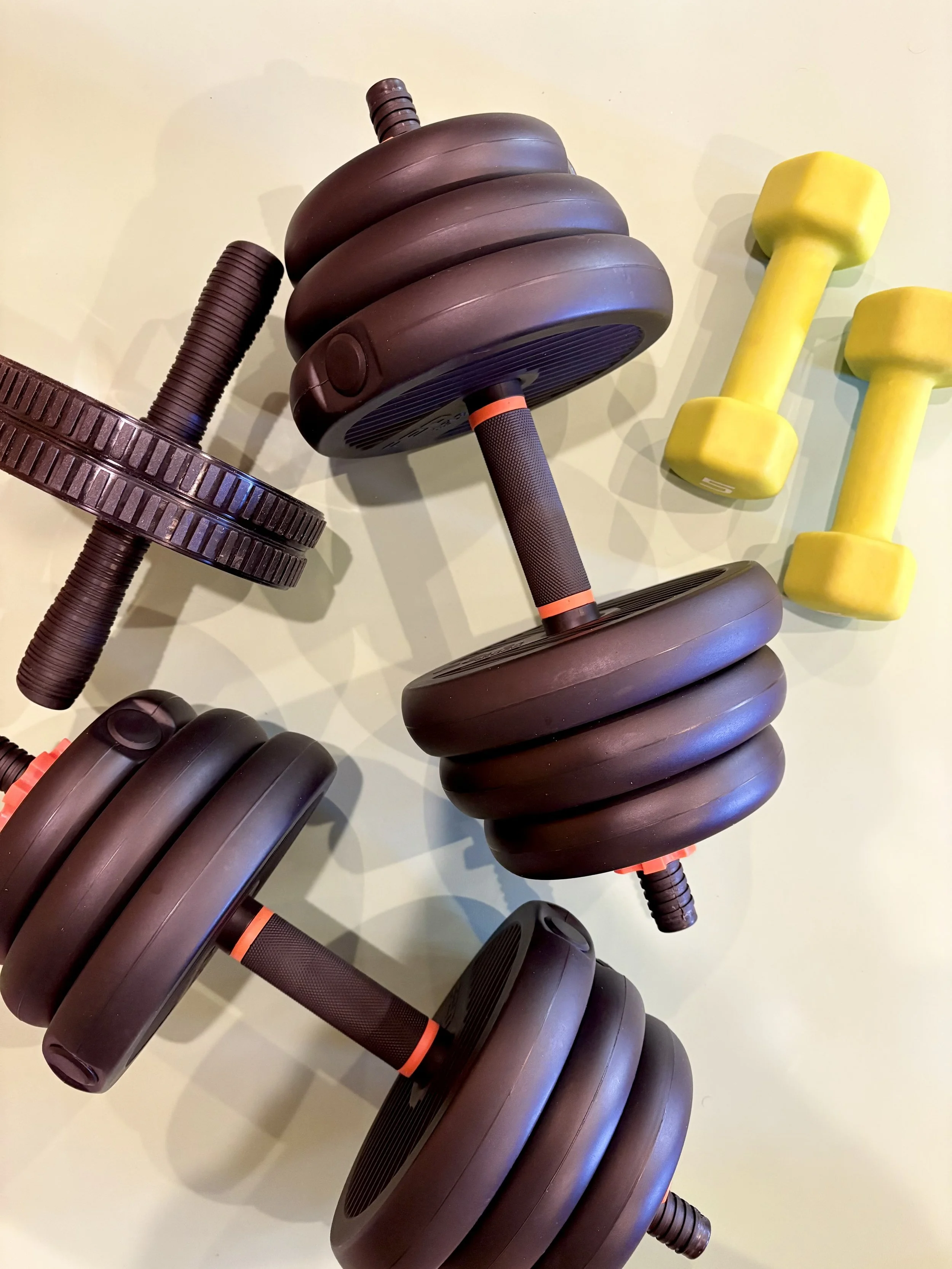 Various black and yellow dumbbells and weight plates on a light-colored surface.