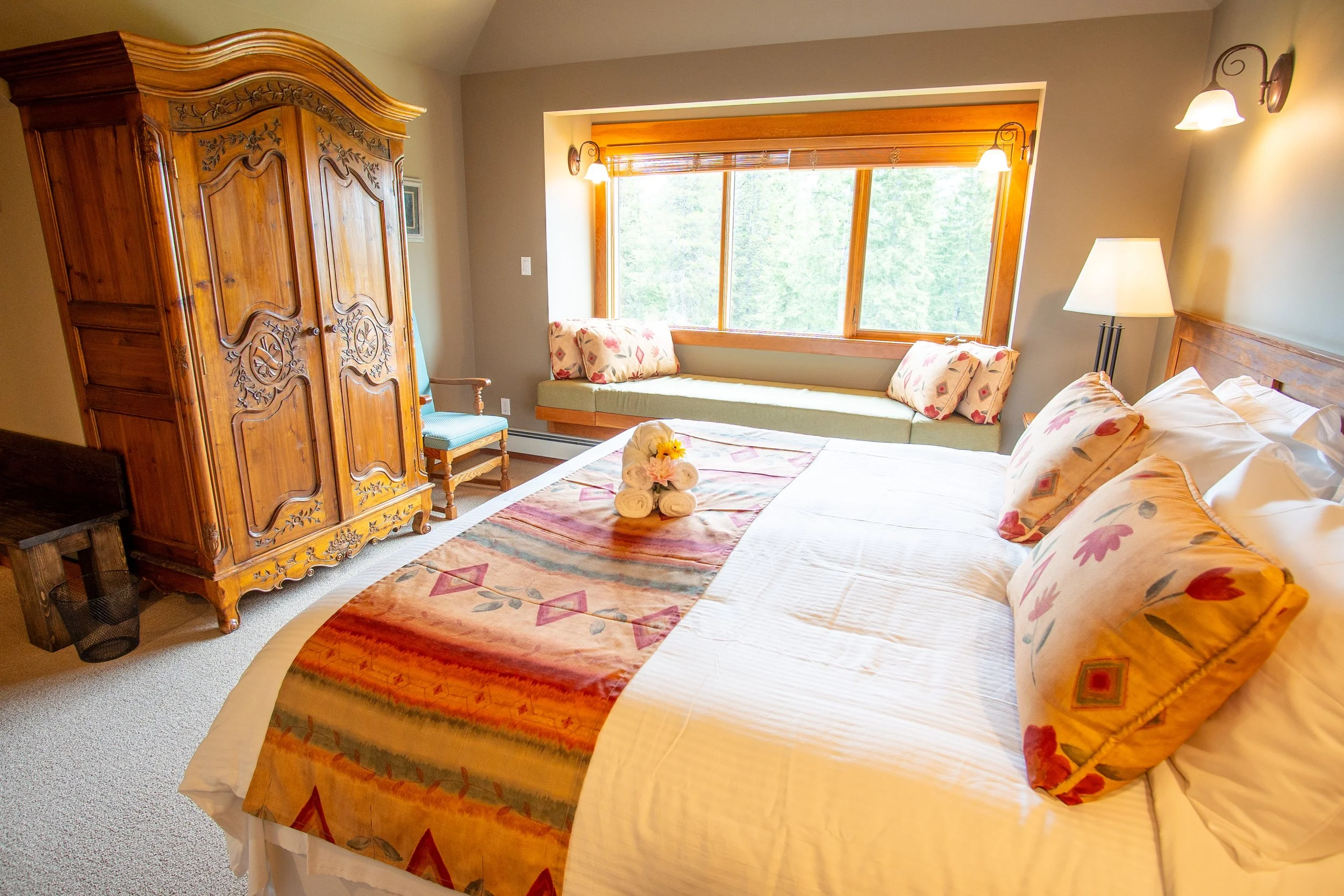 Hotel room with a bed, nightstand, lamps, framed picture, window with blinds, and wooden furniture.