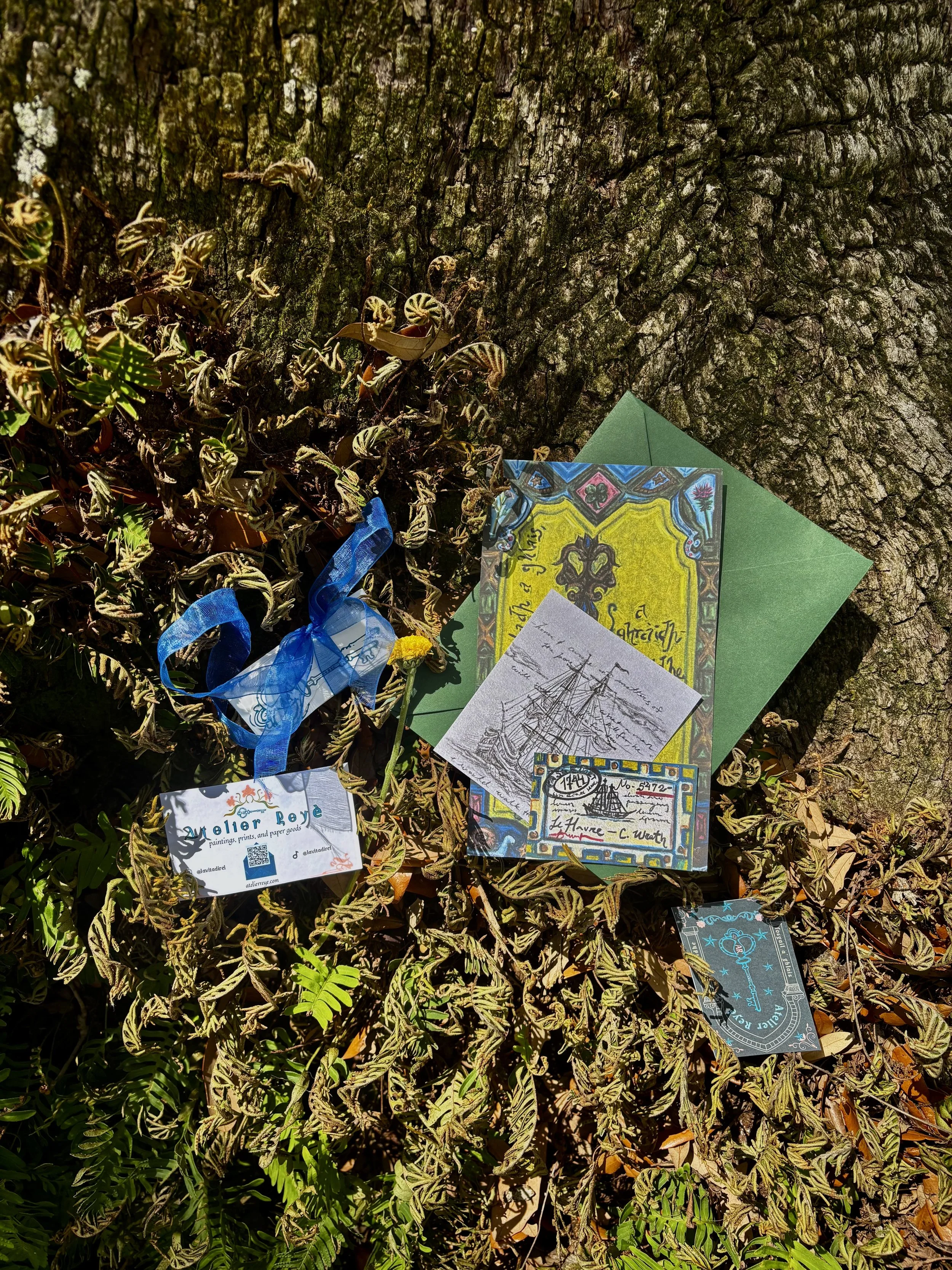 Various art prints and notes placed on a tree trunk with green foliage around.