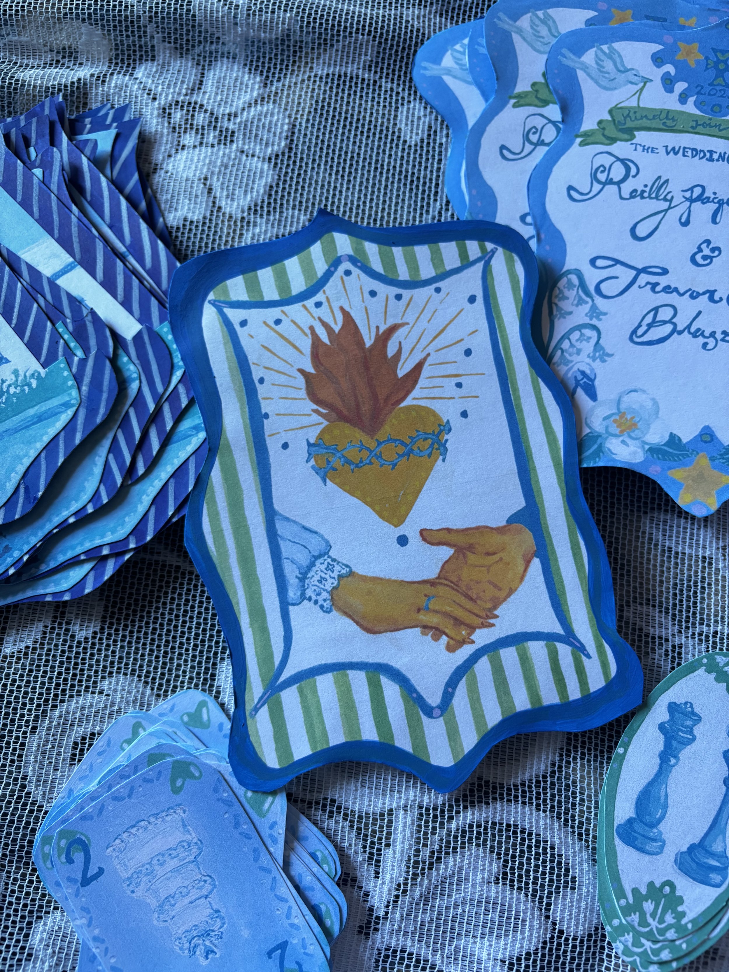 Colorful wedding or celebration programs with handwritten text and illustrations, placed on a lace tablecloth.