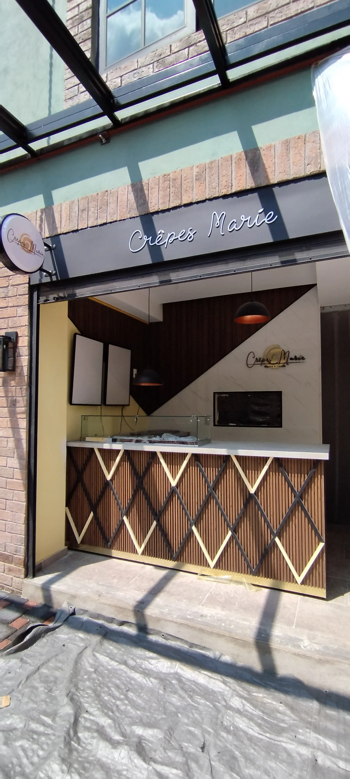 A storefront with a sign that reads 'Crêpes Marie' and a small counter inside, surrounded by brick and pastel green exterior walls.