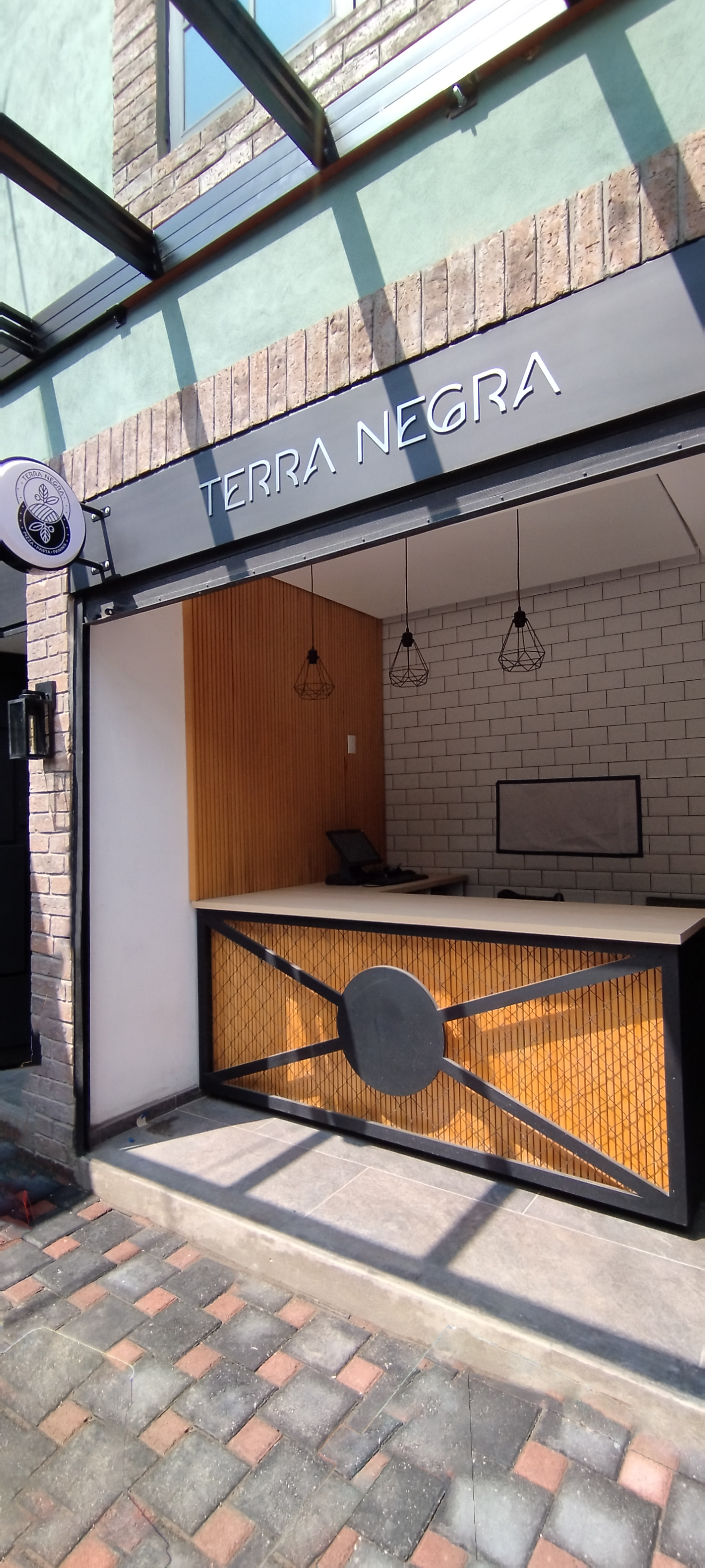 The exterior of a business named Terra Negra with a small entrance area featuring a counter, wood paneling, wire design accents, and hanging geometric light fixtures.
