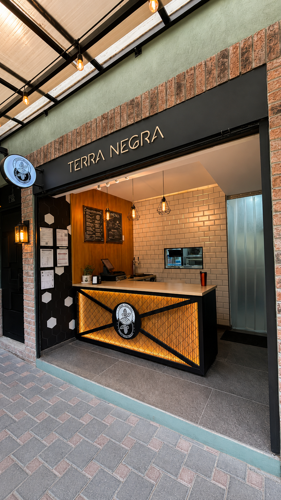 Vista frontal del local llamado Terra Negra, con decoración moderna, iluminación cálida y paredes de ladrillo y azulejo blanco.
