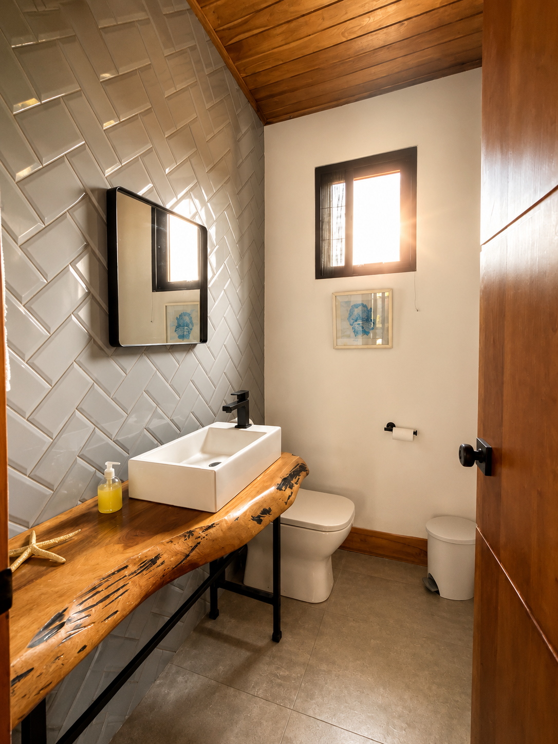 Bathroom with wooden countertop, square vessel sink, black faucet, wall mirror, and decor, finished with wood, tile, and a small window letting in sunlight.