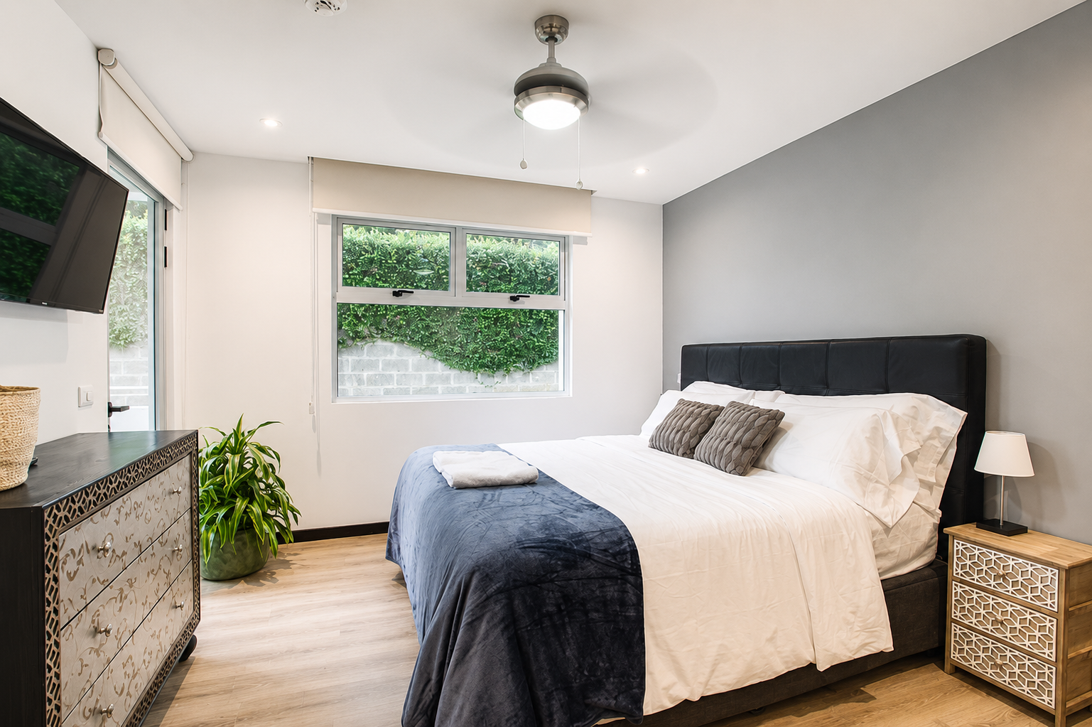 A bedroom with a bed, window, TV, and dresser