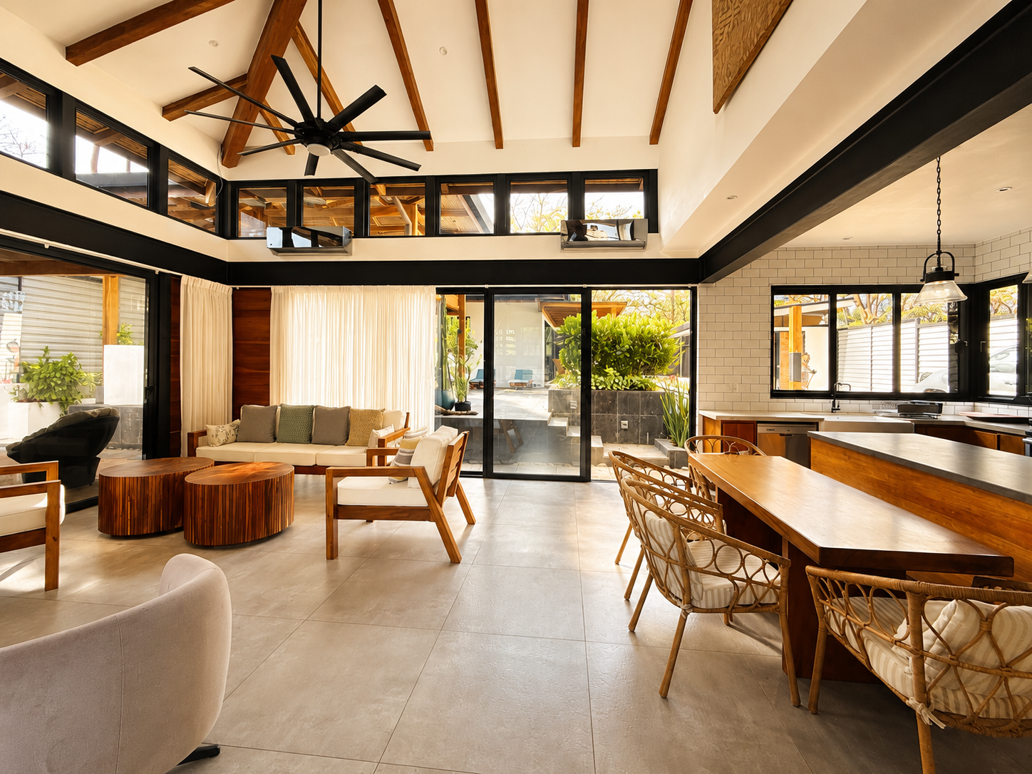 Open-concept living room and kitchen with wooden beams, large windows, and modern furniture.