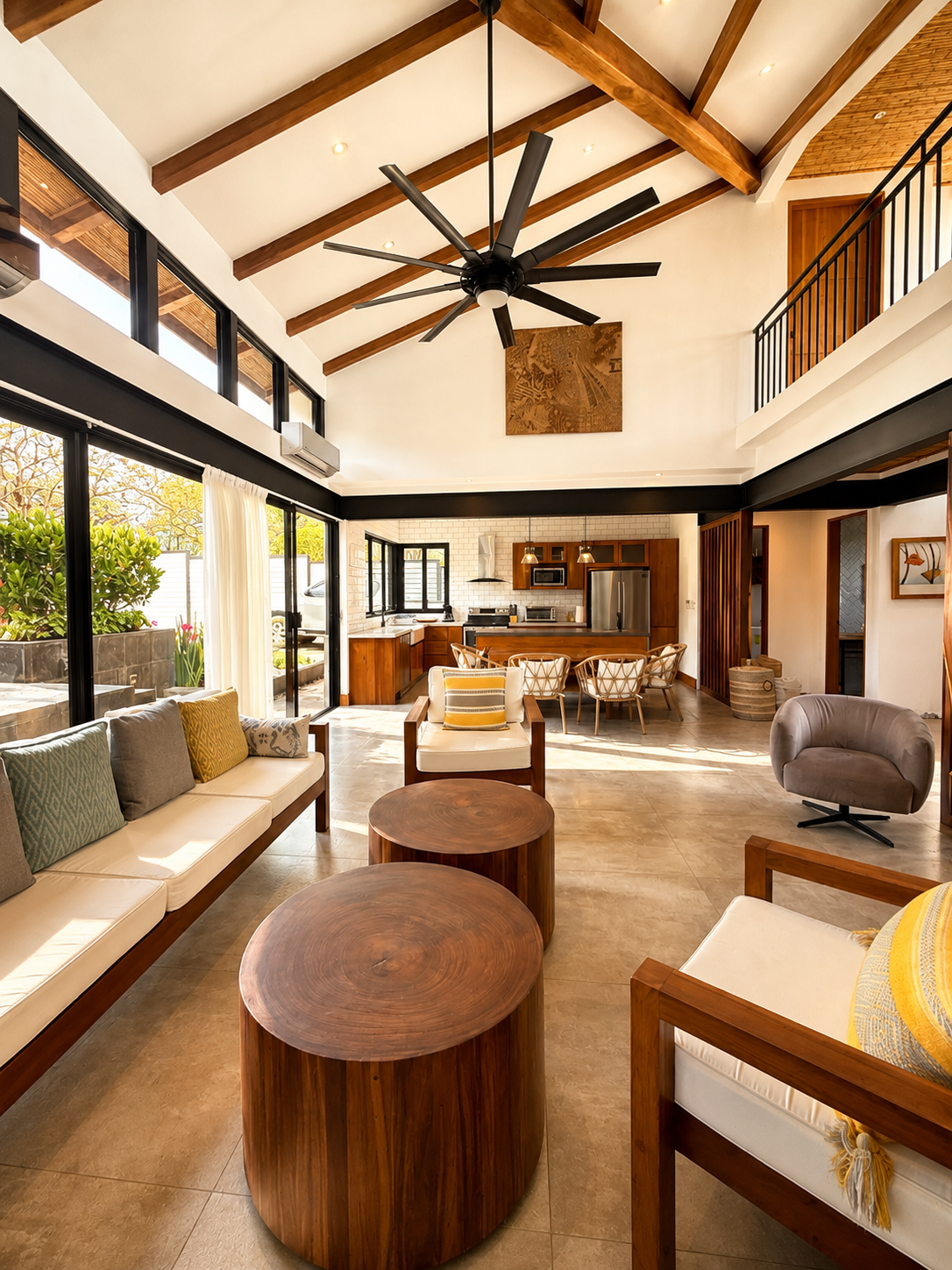 Open-concept living room and kitchen with high vaulted ceiling, wooden beams, ceiling fan, large windows, and modern furniture
