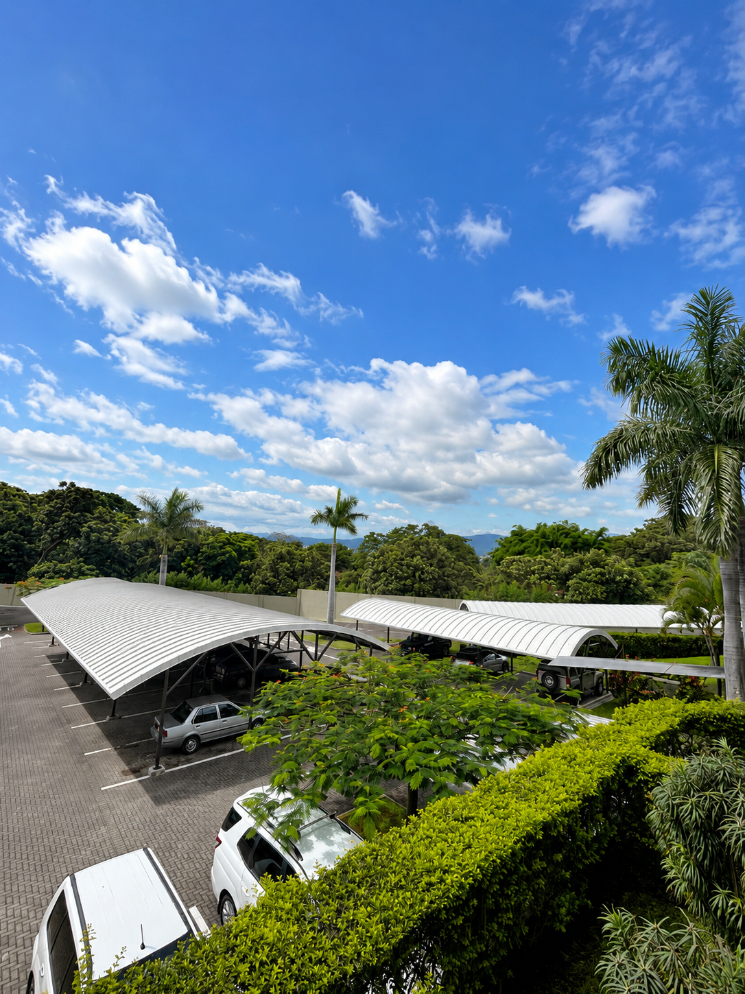 Parking lot with white canopies, green trees, and a blue sky with clouds.