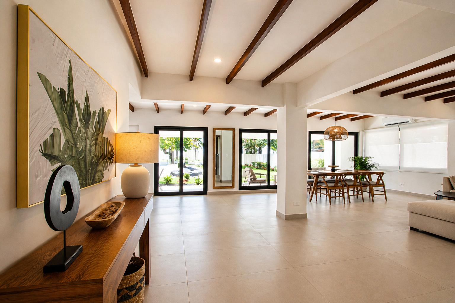 Spacious, modern living room with large windows, wooden ceiling beams, a dining area with wooden table and chairs, a beige sofa, a large wall art, and a console table with a lamp and decorative items.
