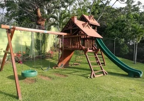 A wooden playset with a slide and swings in a backyard with green grass and trees.