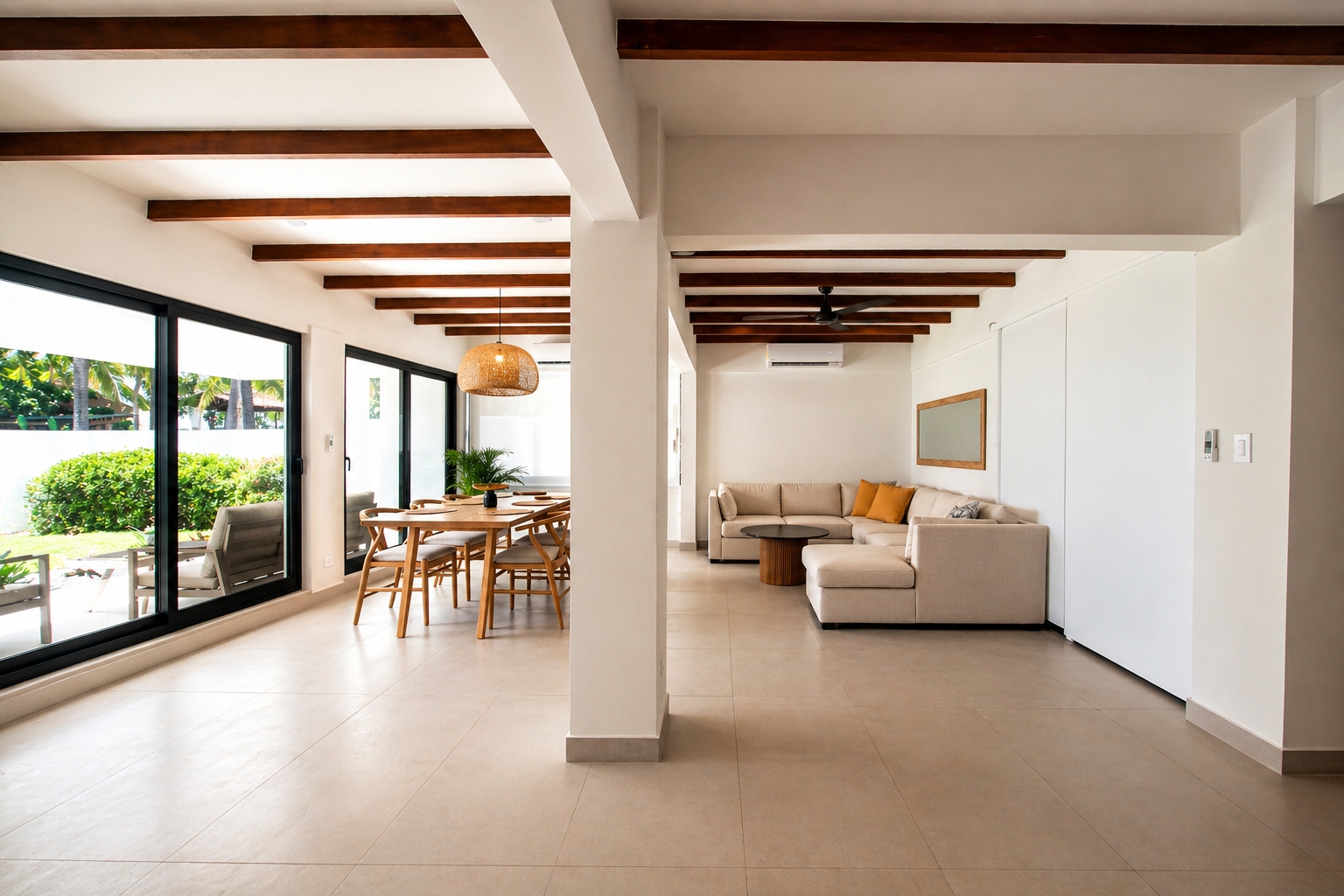 Open-concept living and dining room with large sliding glass doors, wooden beams, beige tiled floor, white walls, and modern furniture including a beige sectional sofa, a wooden dining table with chairs, and indoor plants.