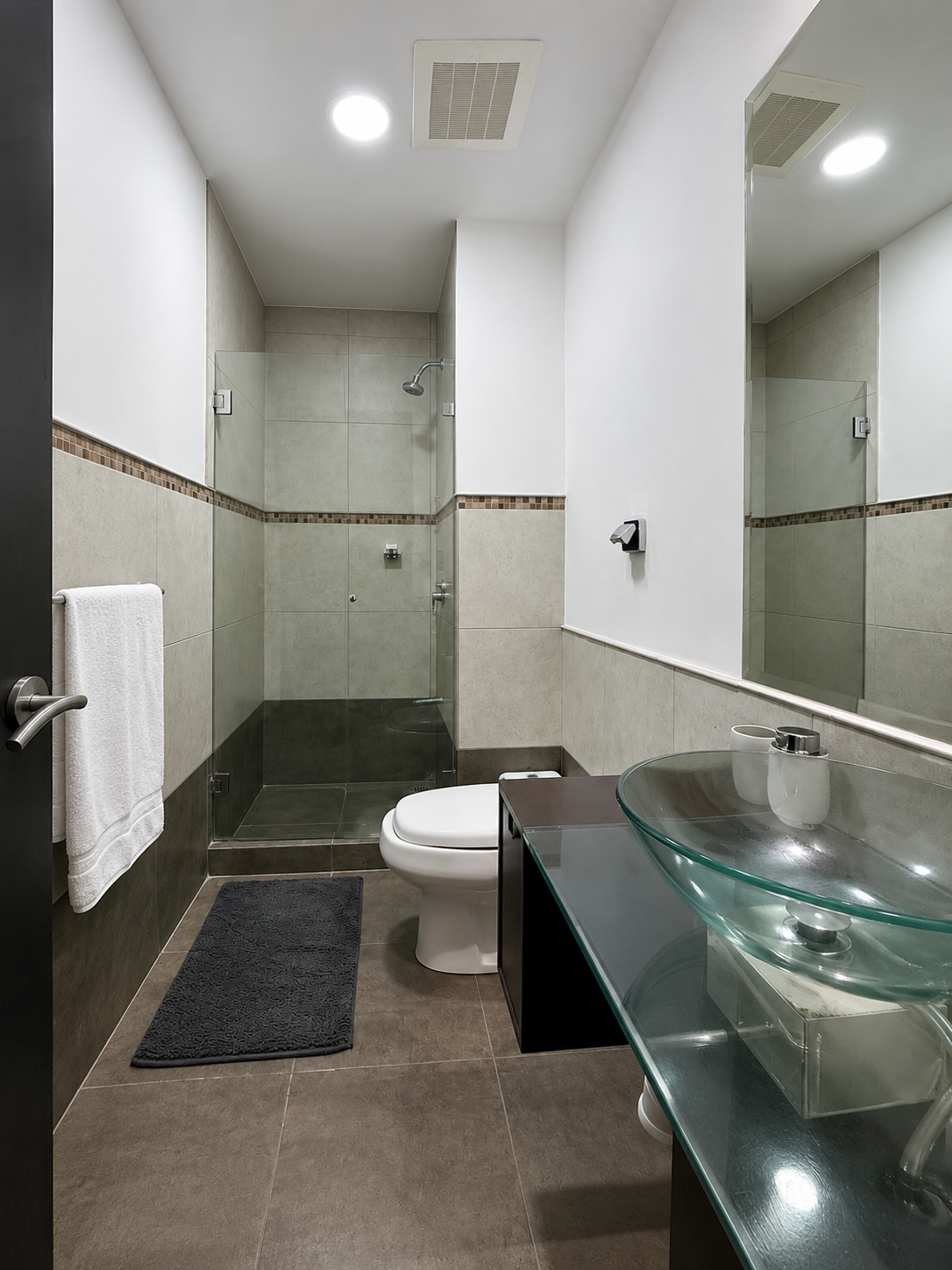 Modern bathroom with a walk-in shower, toilet, glass sink, large mirror, and white walls.
