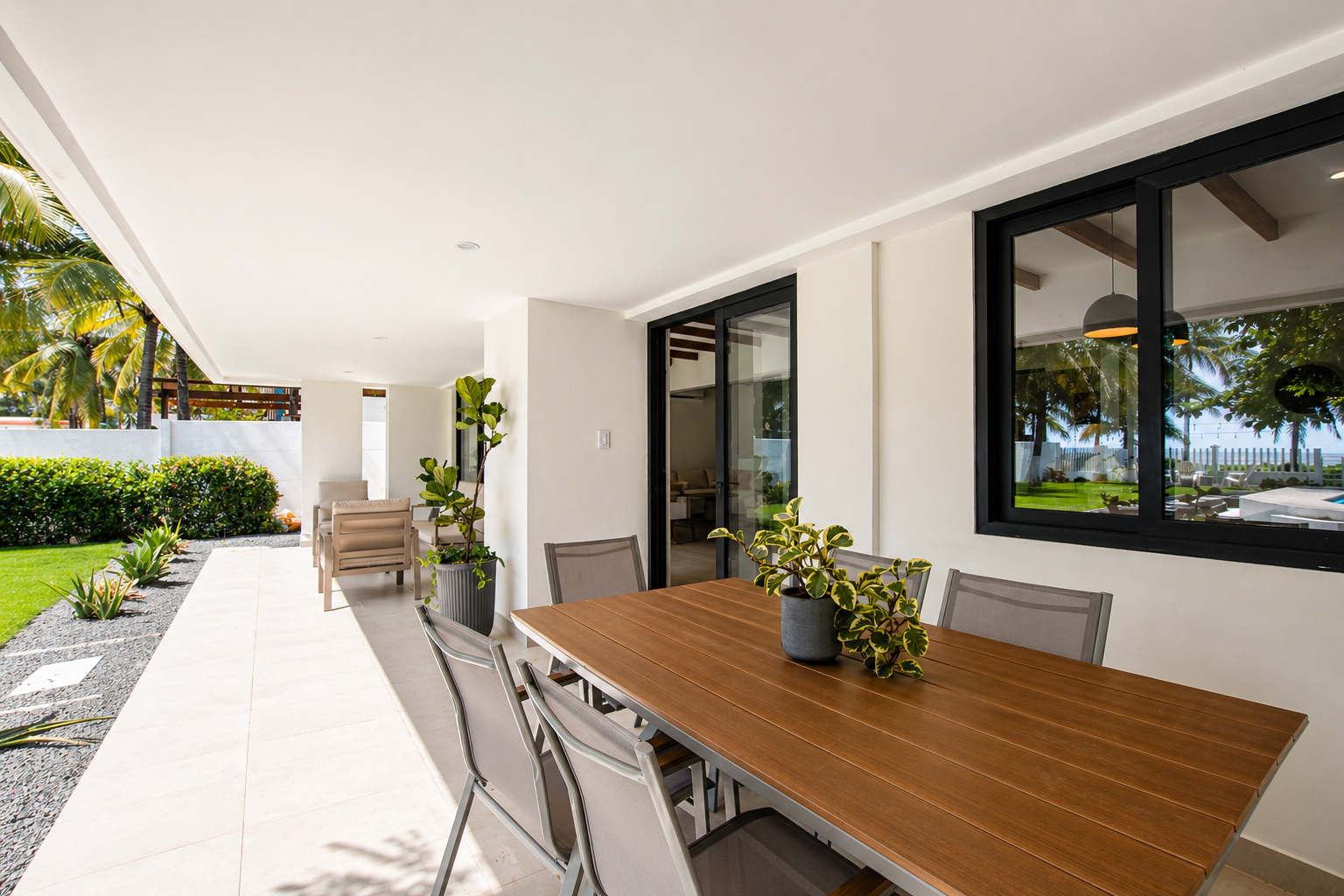 Outdoor patio with wooden dining table, potted plants, and outdoor seating area, surrounded by lush greenery.