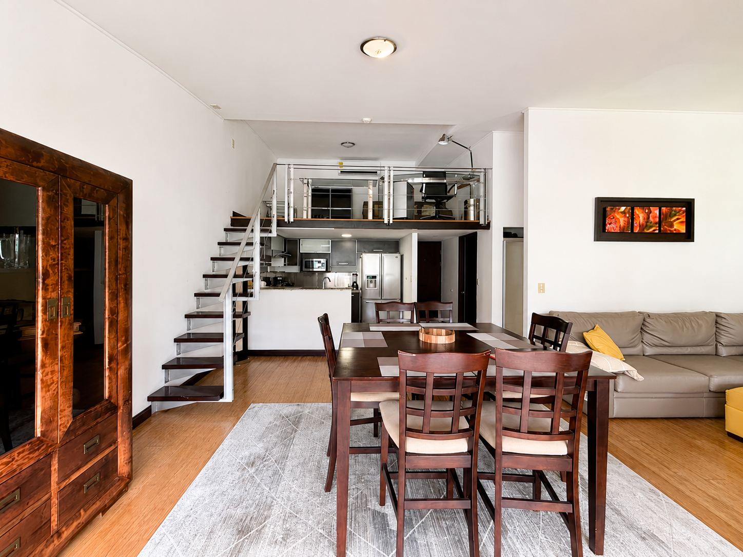 Open-concept living and dining area with staircase, kitchen, and loft space in a modern apartment.