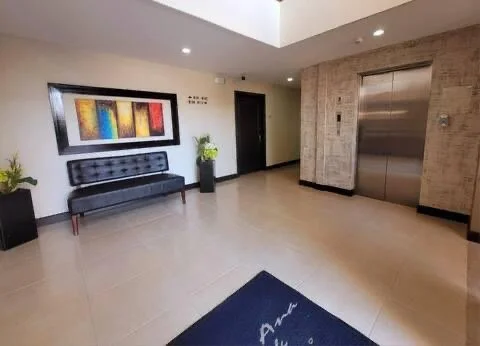 Lobby with a black bench, a colorful abstract painting, potted plants, an elevator, and a door.