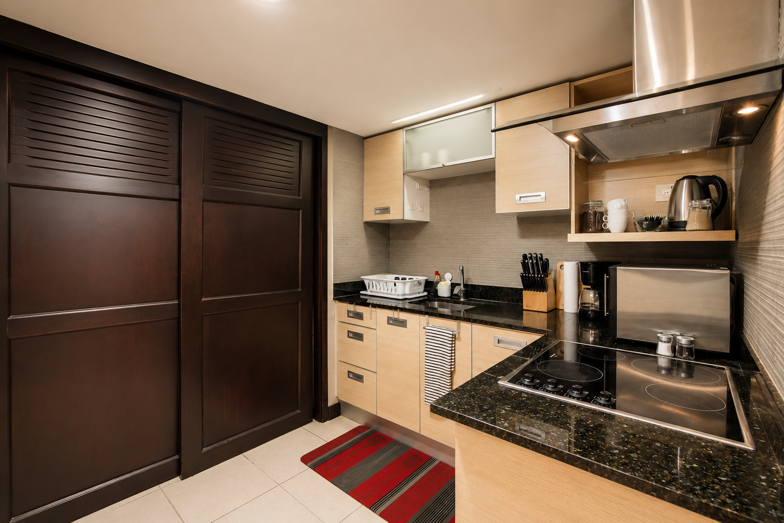 Modern kitchen with light wood cabinets, black granite countertops, stainless steel appliances, and dark wood sliding door.
