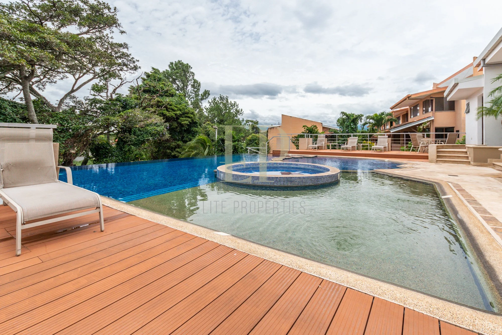 A backyard with a swimming pool, poolside lounge chairs, and trees surrounding the area under a partly cloudy sky.