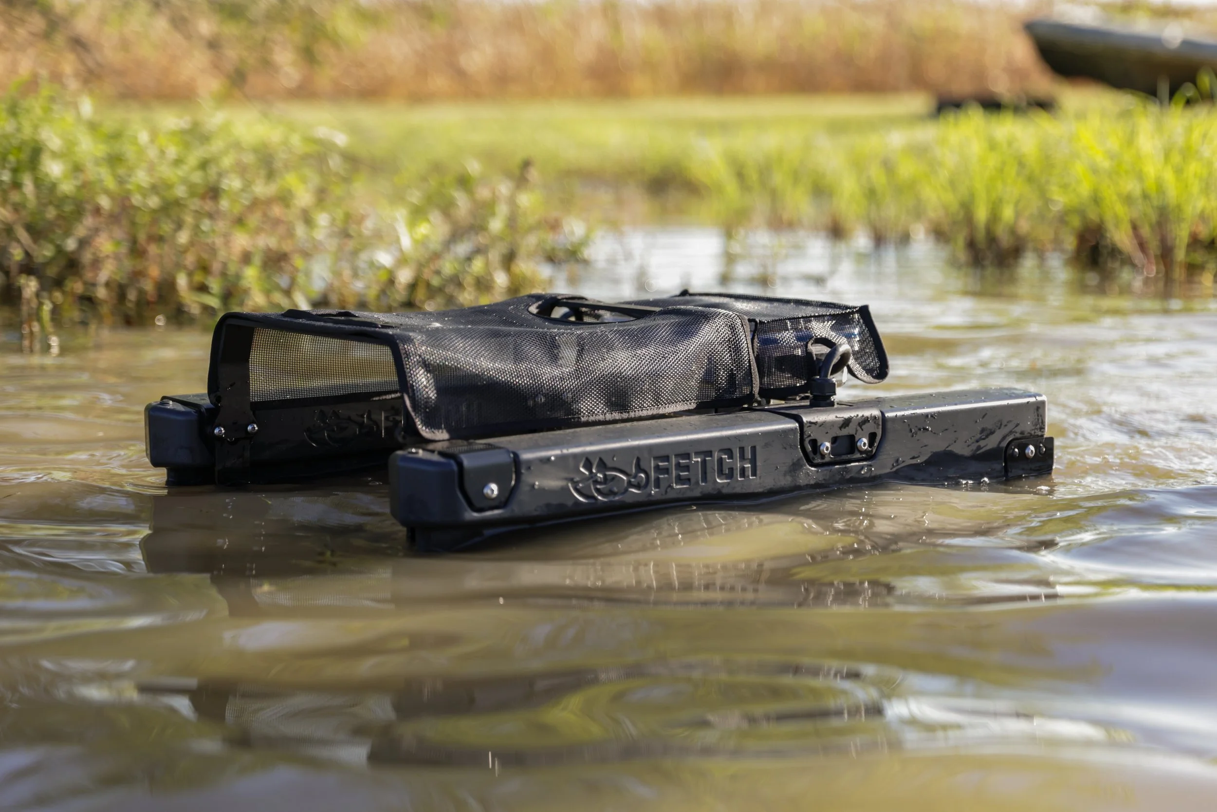 A Fetch waterfowl retrieval system floating on water, surrounded by green grass and plants.