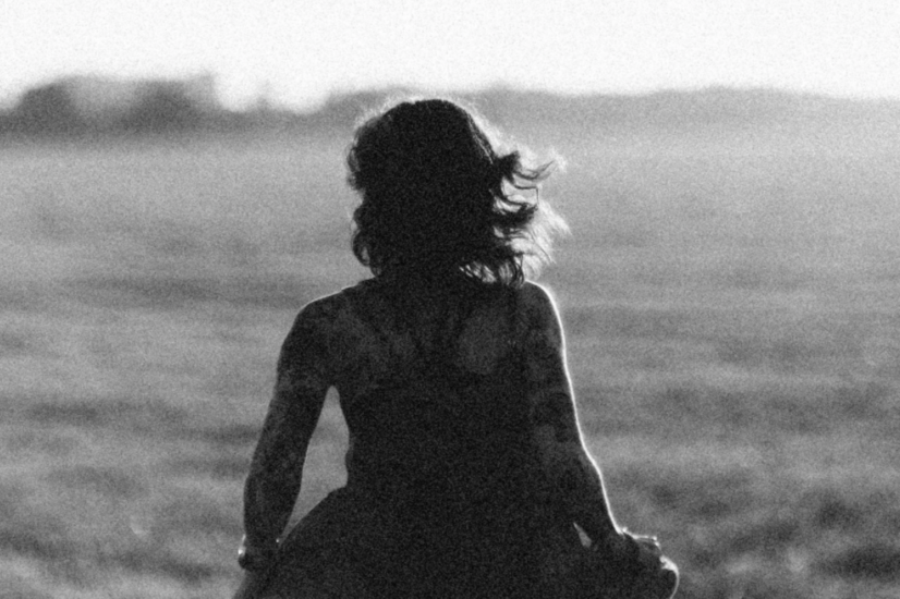 A silhouette of a woman with long hair sitting on a beach, facing the ocean in black and white.