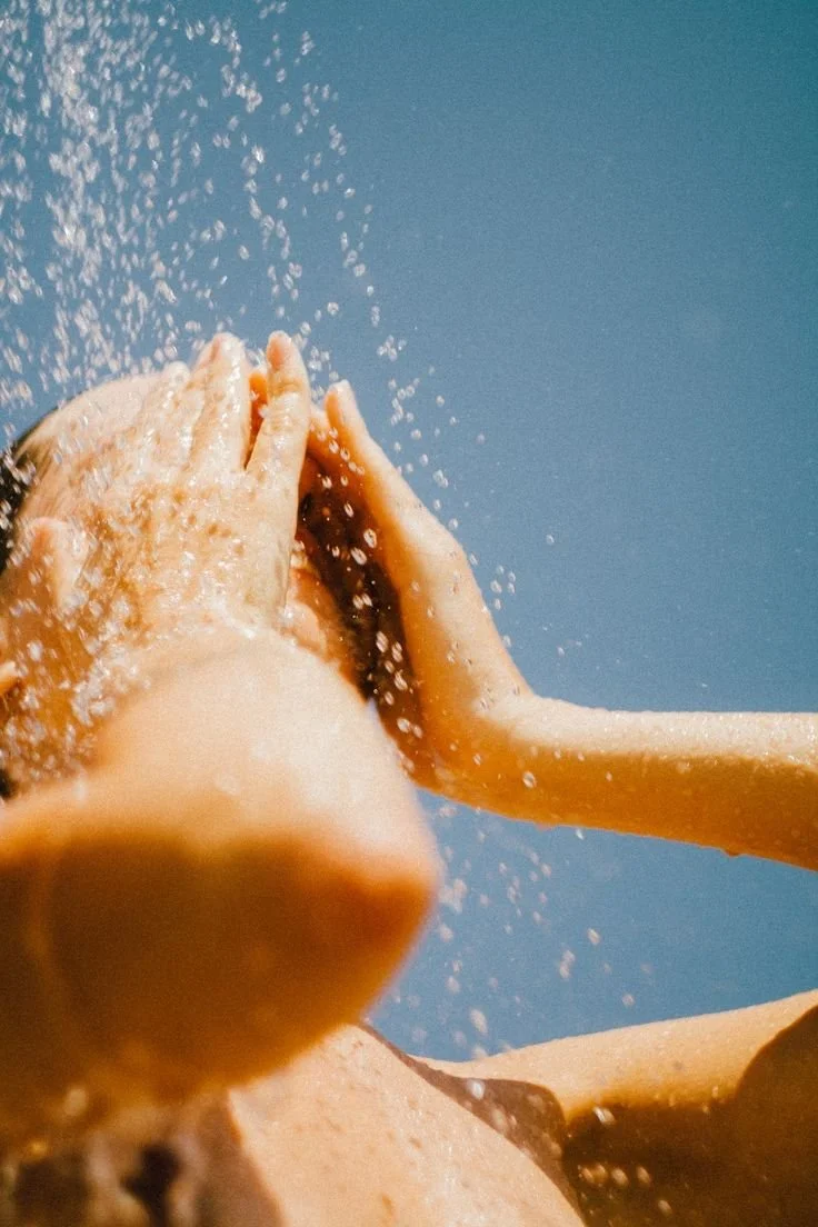 Close-up of a person rinsing their hands under running water with soap, on a blue background.