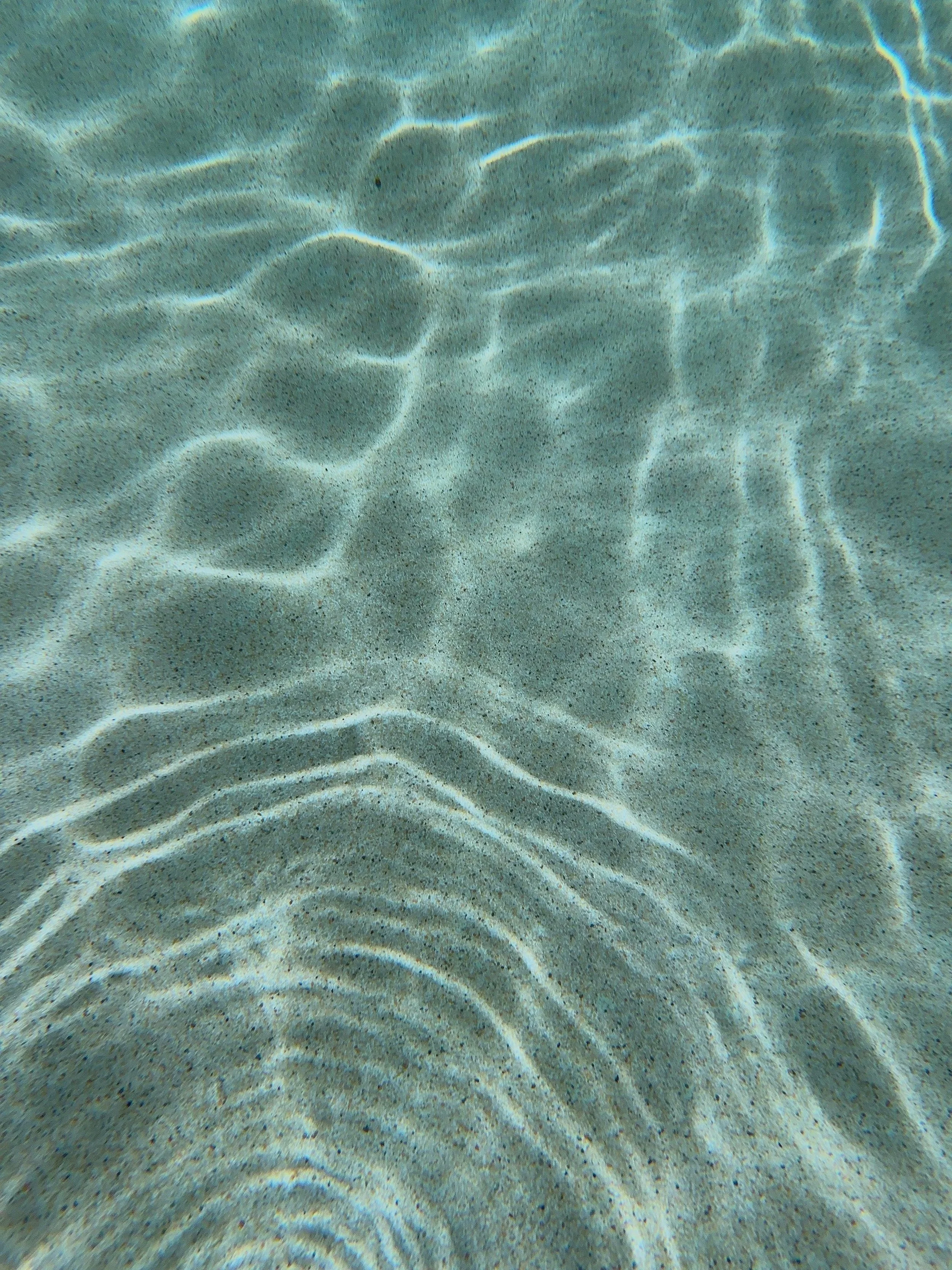 Underwater view of sandy ocean floor with light reflecting off the surface.