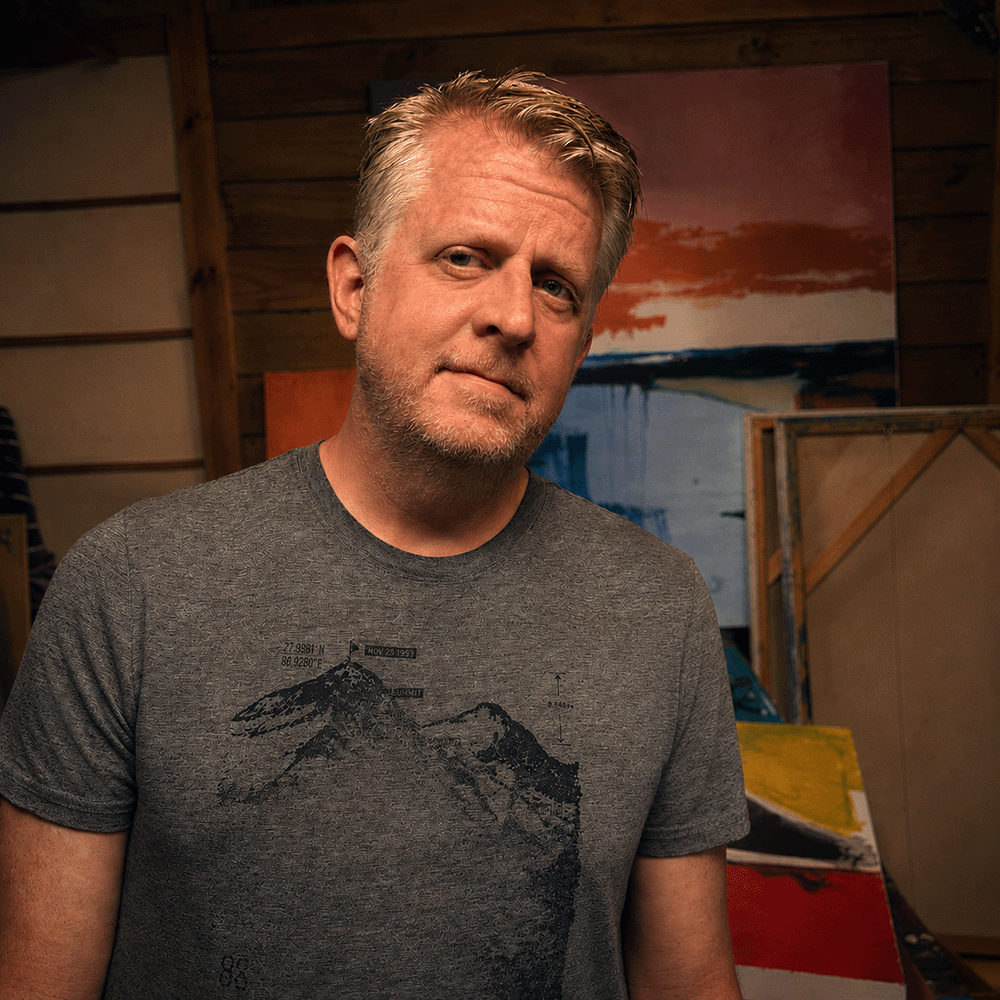 Dean Sauls in his art studio with paintings and canvases in the background.