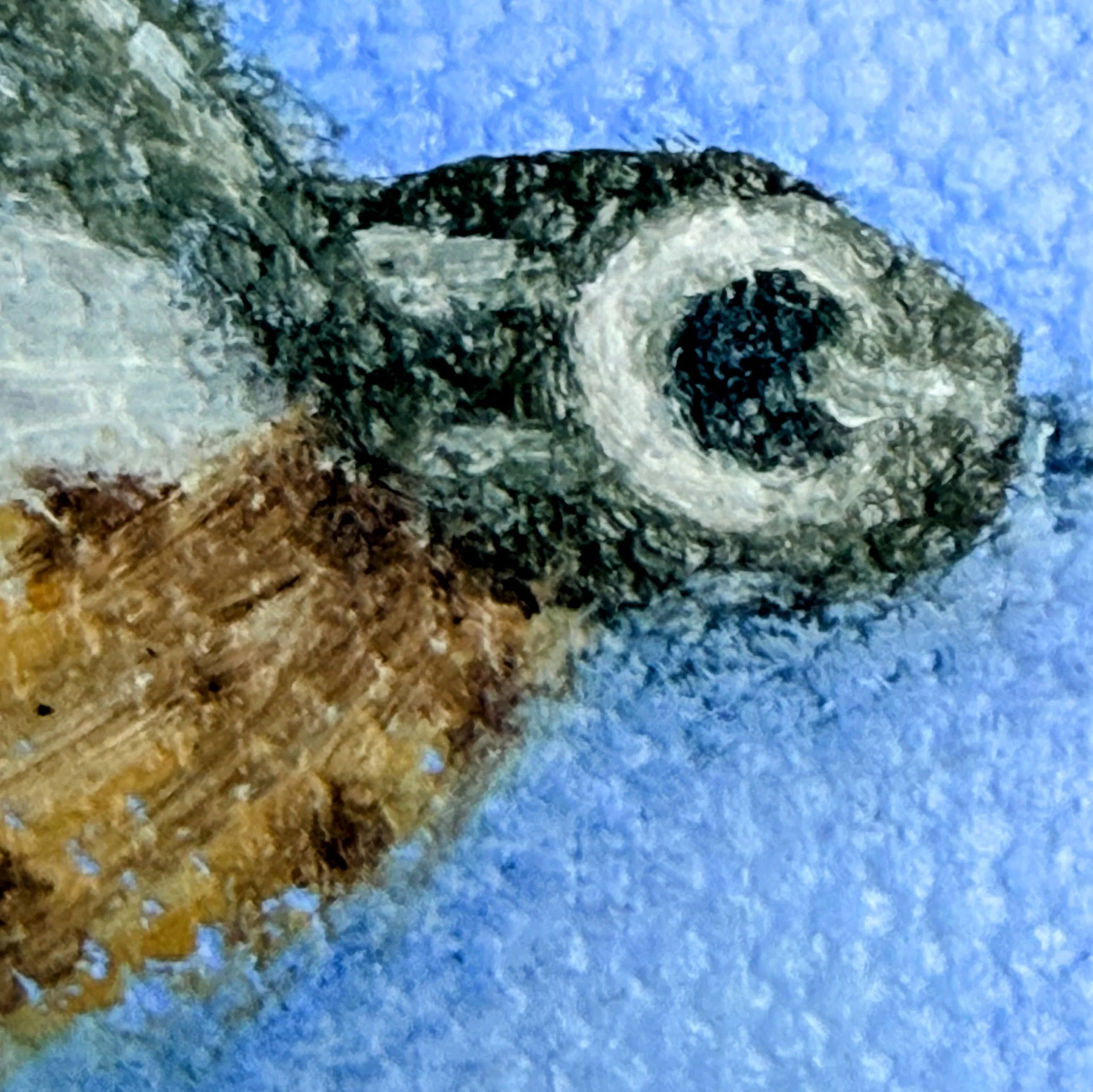 Close-up of a miniature fishing fly painted in oil with translucent white feather-like brushwork, gray wing detail, warm brown body accents, hook detail, and visible canvas texture.