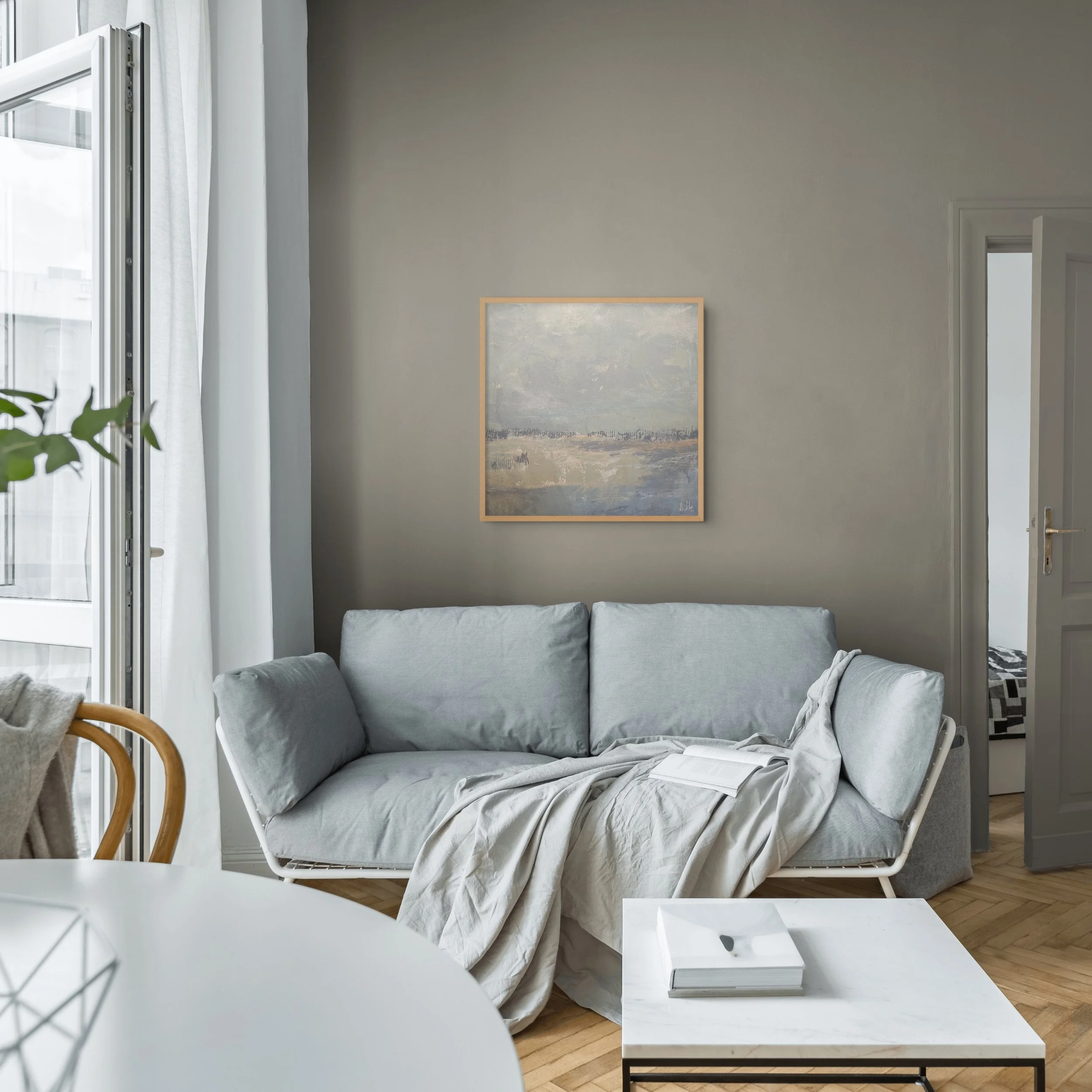 Square abstract landscape painting displayed in a calm modern interior with muted coastal tones, pale neutrals, and layered surface texture.