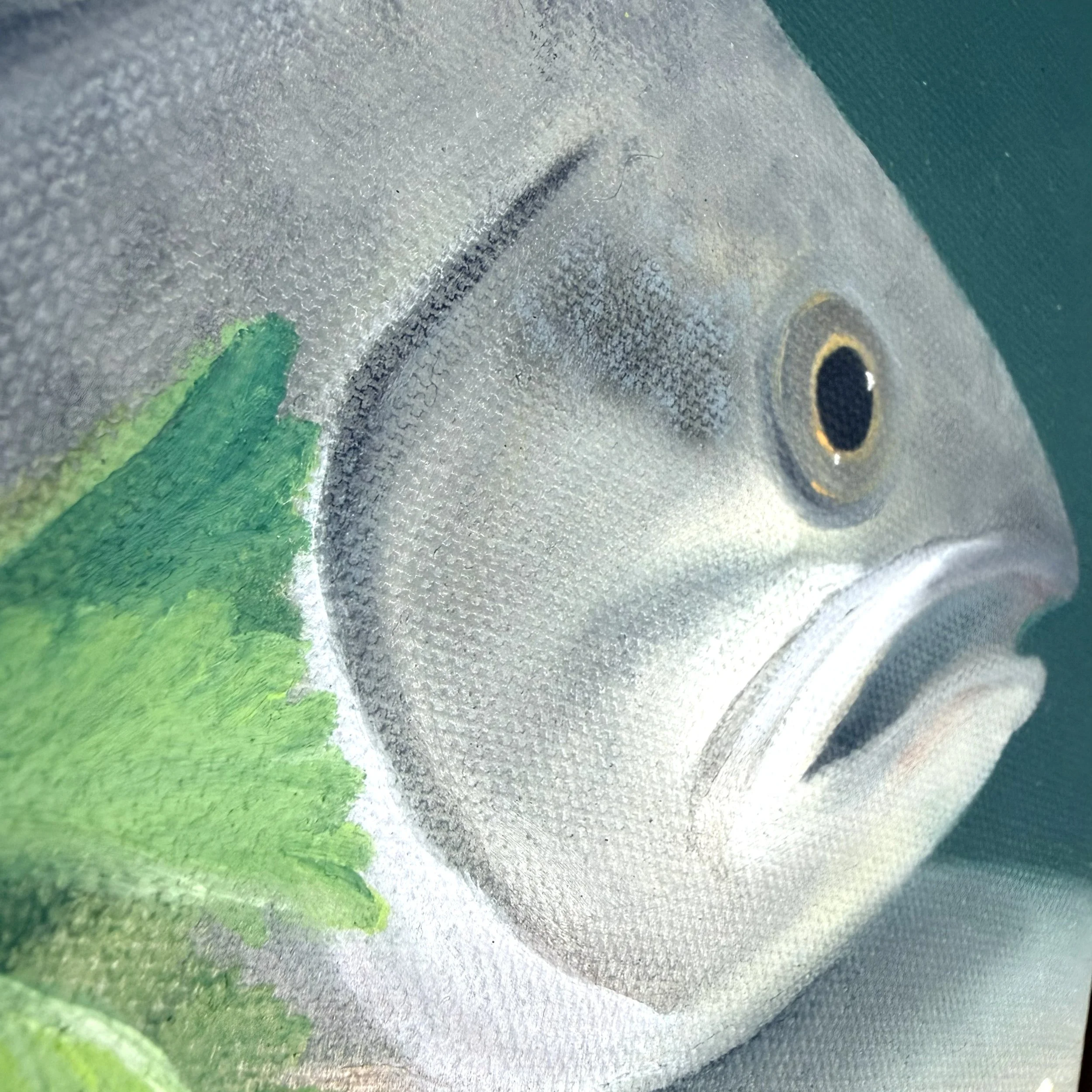 Close-up of a fish still life painted in oil with a bright eye, open mouth, green parsley leaves, yellow lemon wedge, and visible canvas texture.