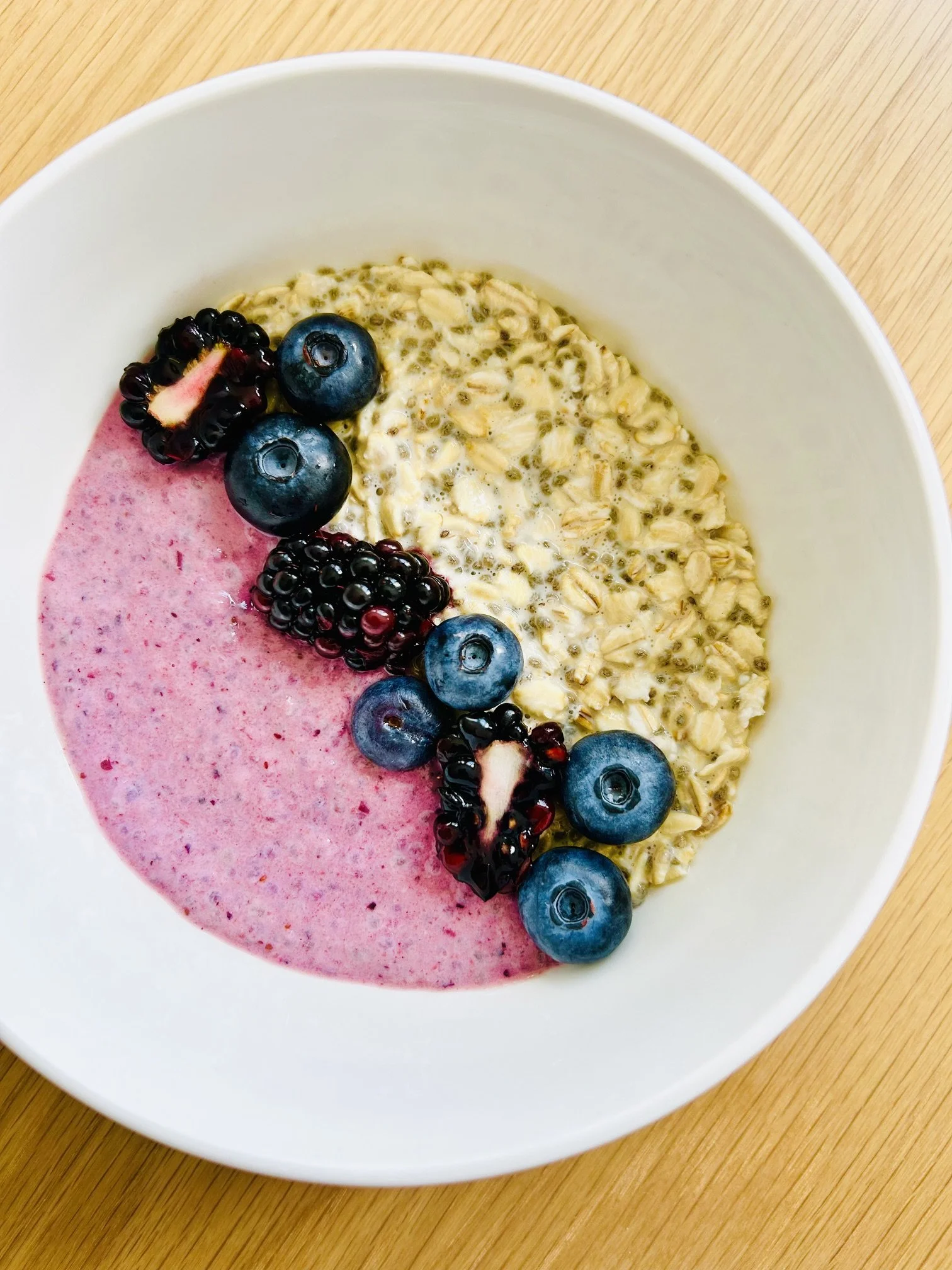 A bowl of oatmeal topped with blueberries, blackberries, and a pink berry smoothie on the side.