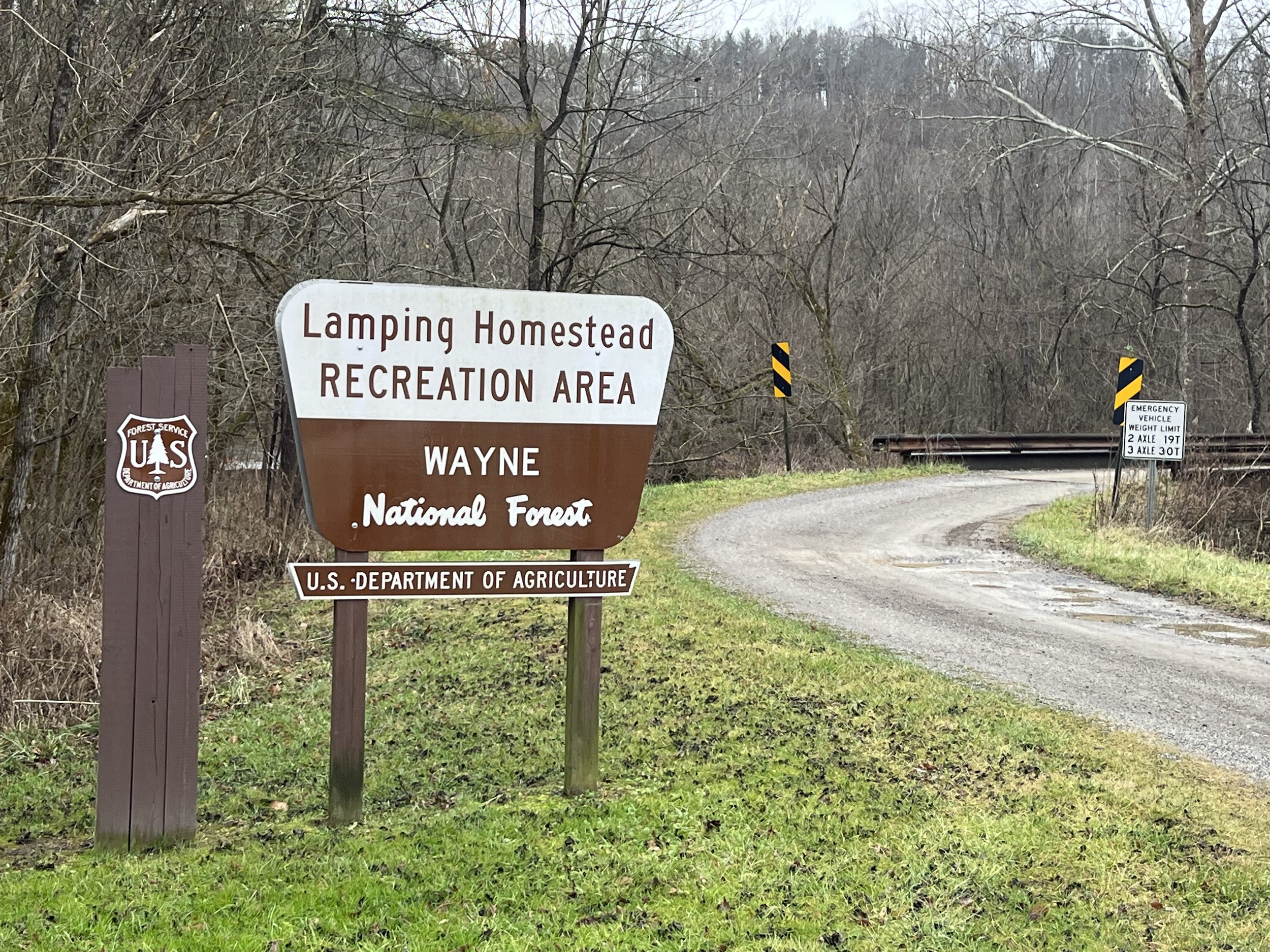 Sign indicating Lantern Homestead Recreation Area located in Wayne National Forest, with trees in the background and a gravel road.