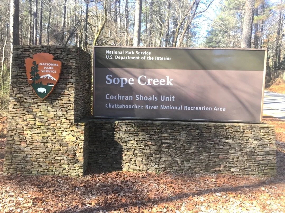 Sign at the entrance of Sope Creek, Cochran Shoals Unit, Chattahoochee River National Recreation Area, managed by the National Park Service, U.S. Department of the Interior, surrounded by trees and leaves on the ground.