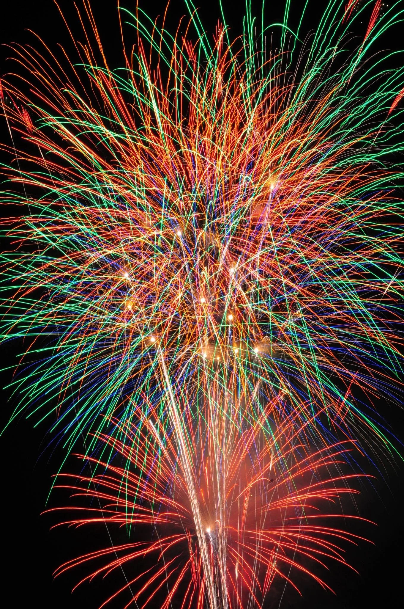 Colorful fireworks bursting in the night sky with red, green, white, and blue streaks radiating outward.