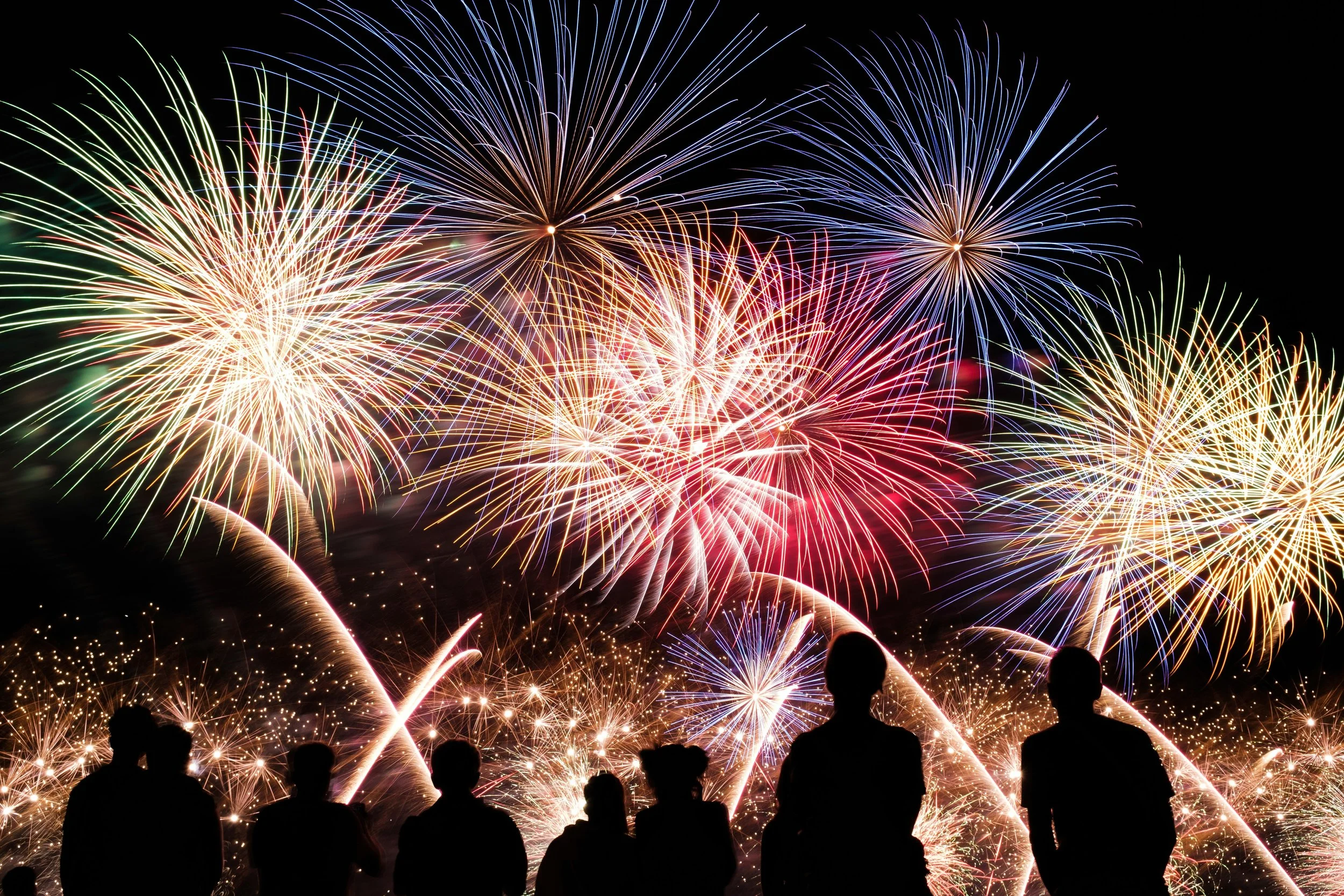 People watching fireworks display at night with colorful explosions in the sky.