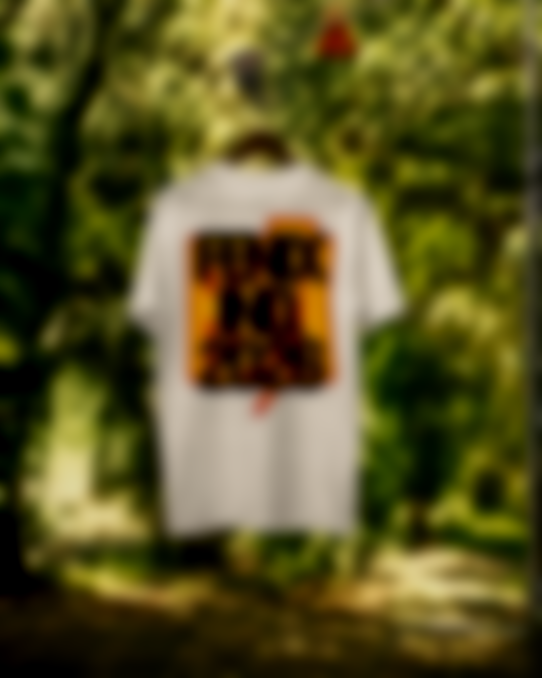 A white t-shirt with a graphic design hangs among green foliage.