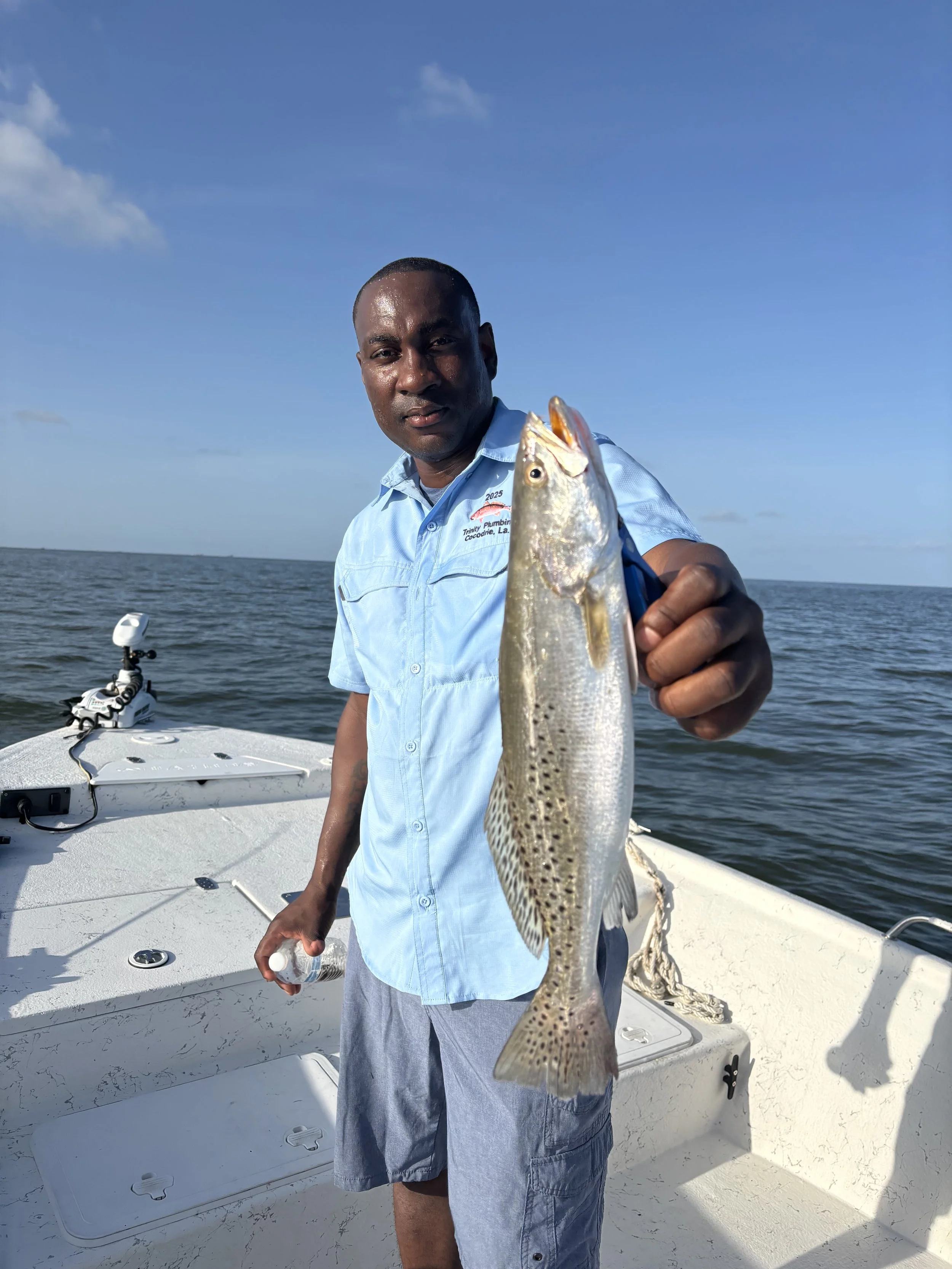 A man on a boat holding a fish he caught, with the ocean and blue sky in the background.