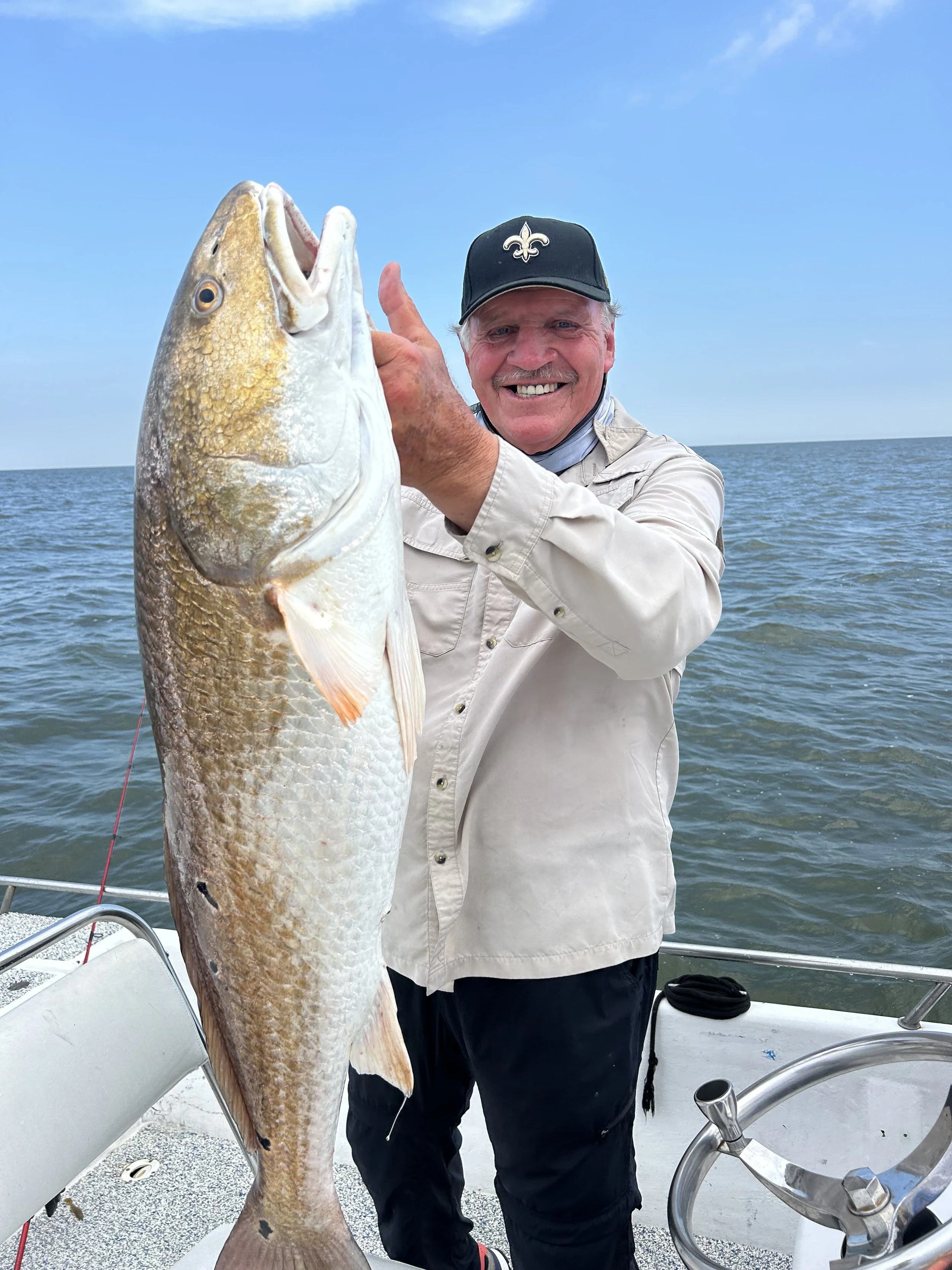 A man smiling and holding a large fish on a boat in the water.