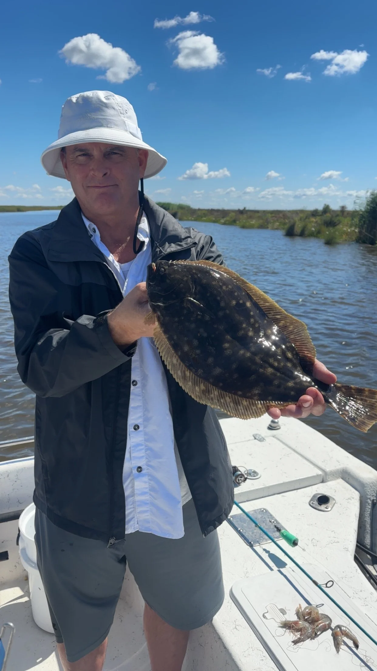 Man on a boat holding a large fish with water and blue sky with clouds in the background.