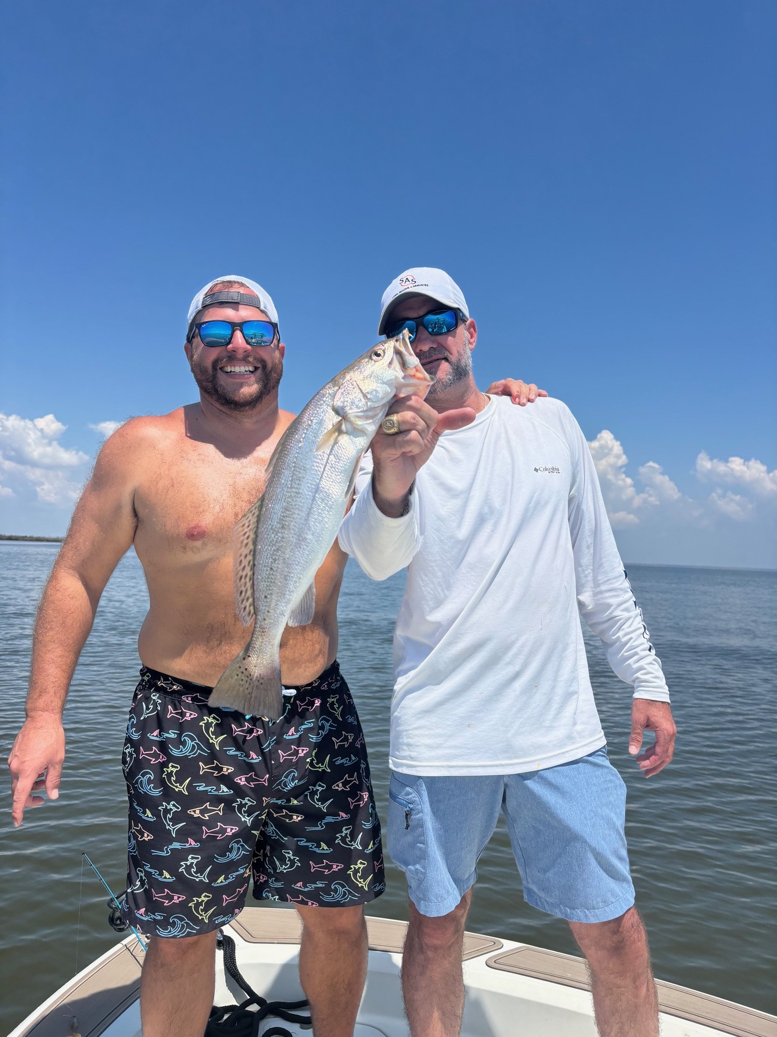 Two men on a boat holding a fish, with water and a blue sky in the background.