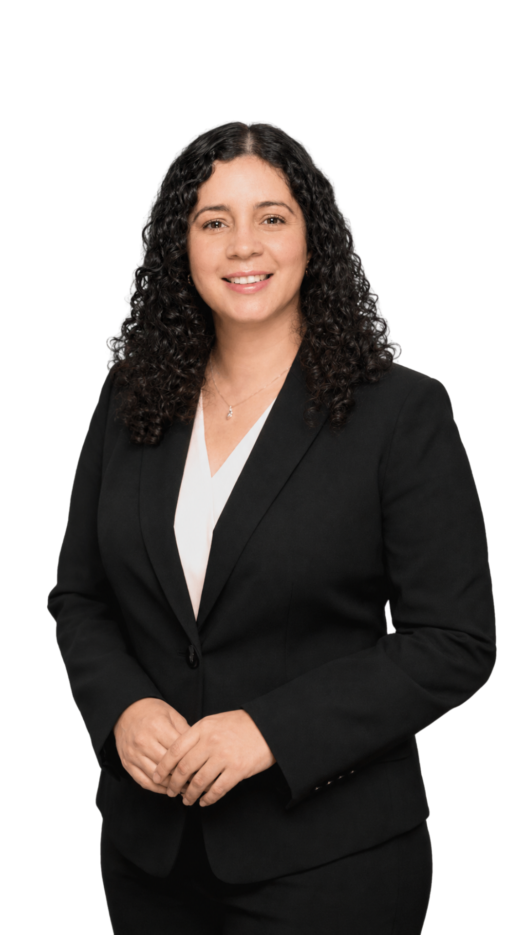 A woman with curly dark hair wearing a black blazer and white top, smiling, standing against a plain background.