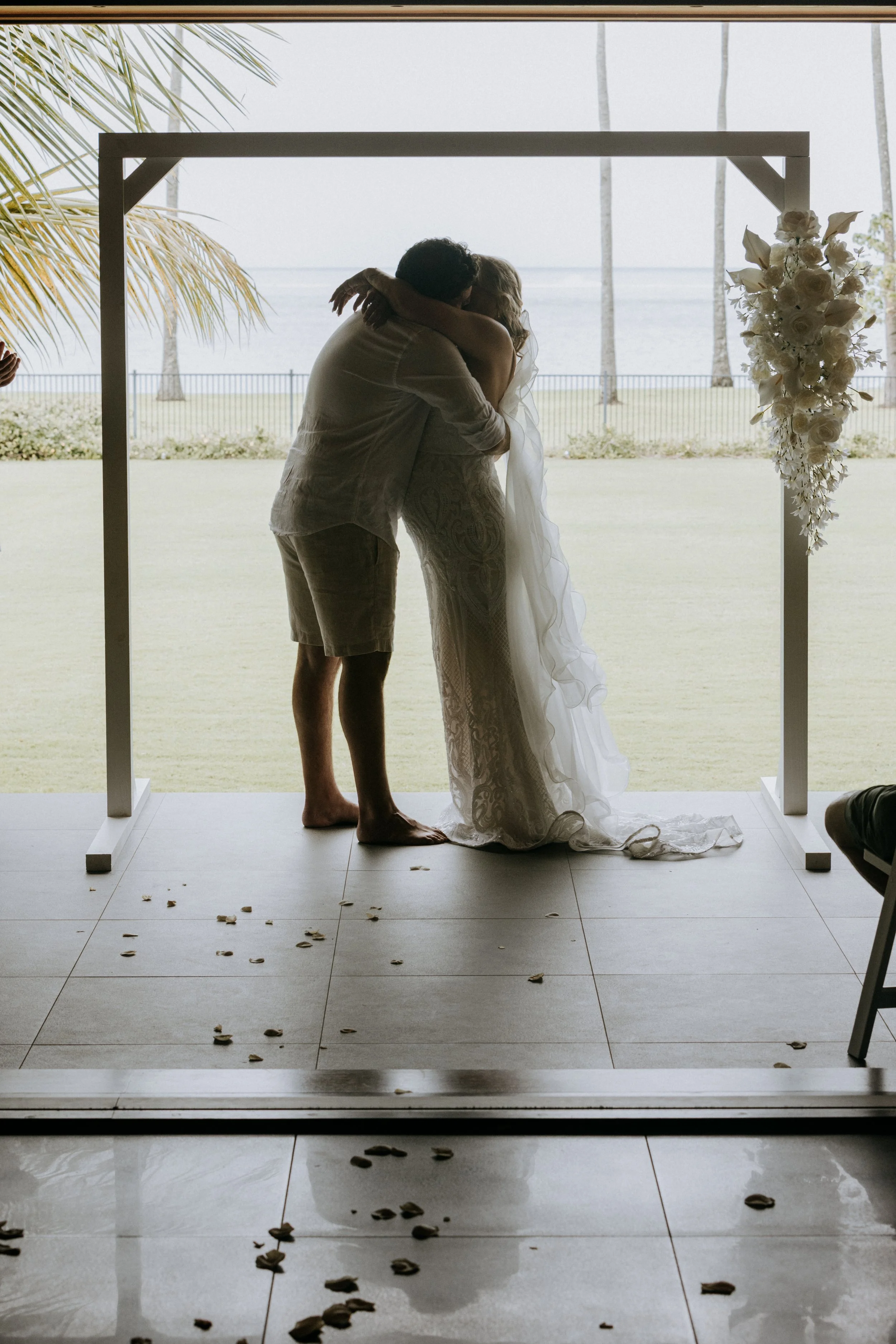 Bride and groom embracing beneath a styled ceremony arbour at Yangaro Resort, with luxury wedding styling by Salt & Silk Collective in the Whitsundays.