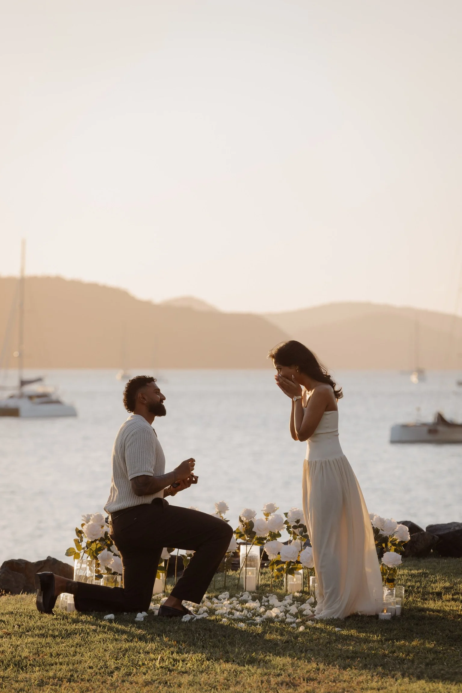 Romantic engagement proposal in Airlie Beach and the Whitsundays featuring waterfront styling, white florals, candles and a luxury proposal experience by Salt & Silk Collective