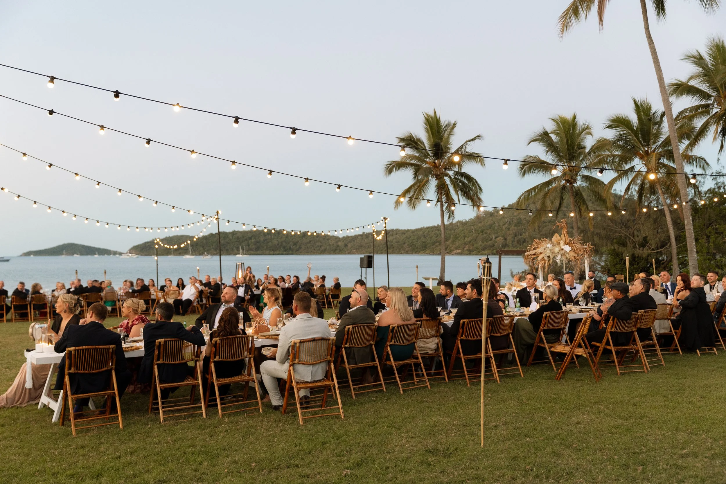 Outdoor wedding reception styling with festoon lighting, bamboo chair hire, tablescapes and coastal event hire in Airlie Beach, Whitsundays by Salt & Silk Collective.