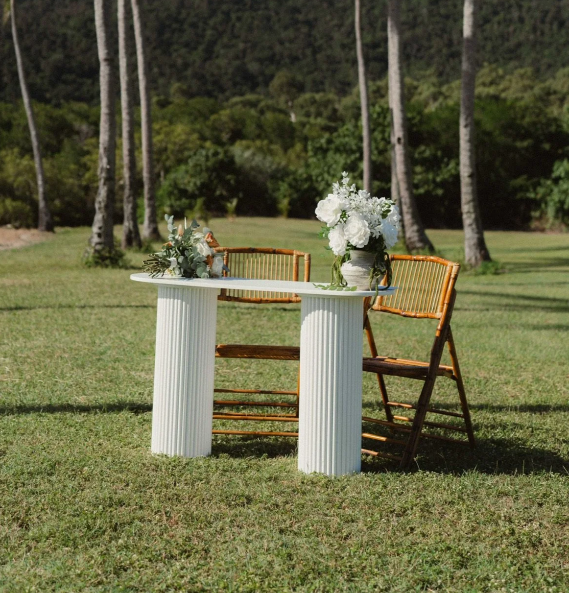 Elegant wedding signing table with white fluted table, bamboo chairs and faux floral arrangements for an outdoor ceremony in Airlie Beach, Whitsundays by Salt & Silk Collective.