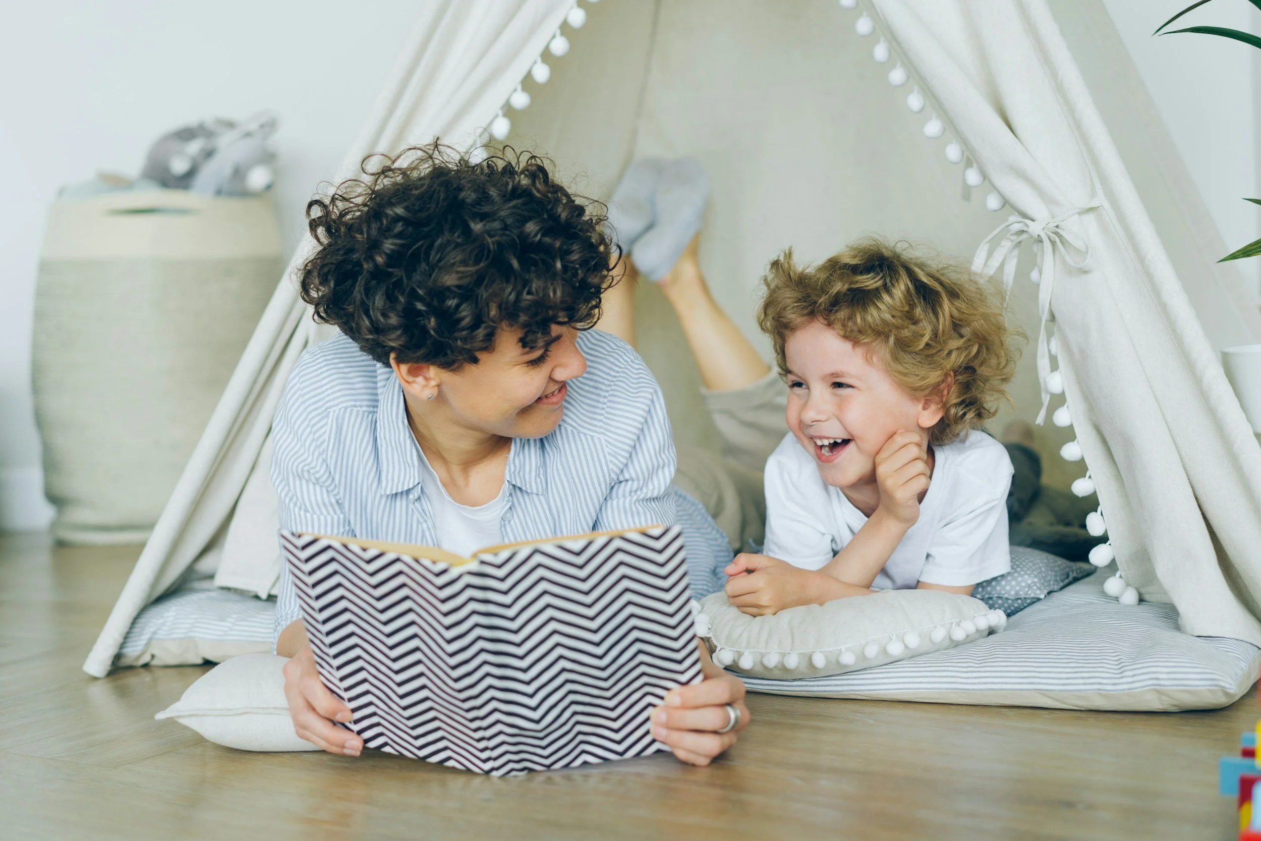 A woman and young boy reading a book together in a play tent