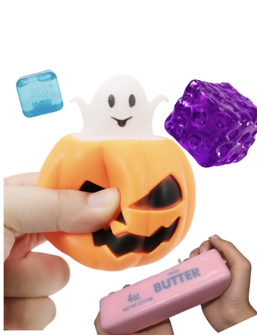 A Halloween-themed toy with a pumpkin shape and a ghost inside, surrounded by colorful objects including a blue cube, a purple textured cube, and a pink bar of butter. Hands are holding the toy and butter.