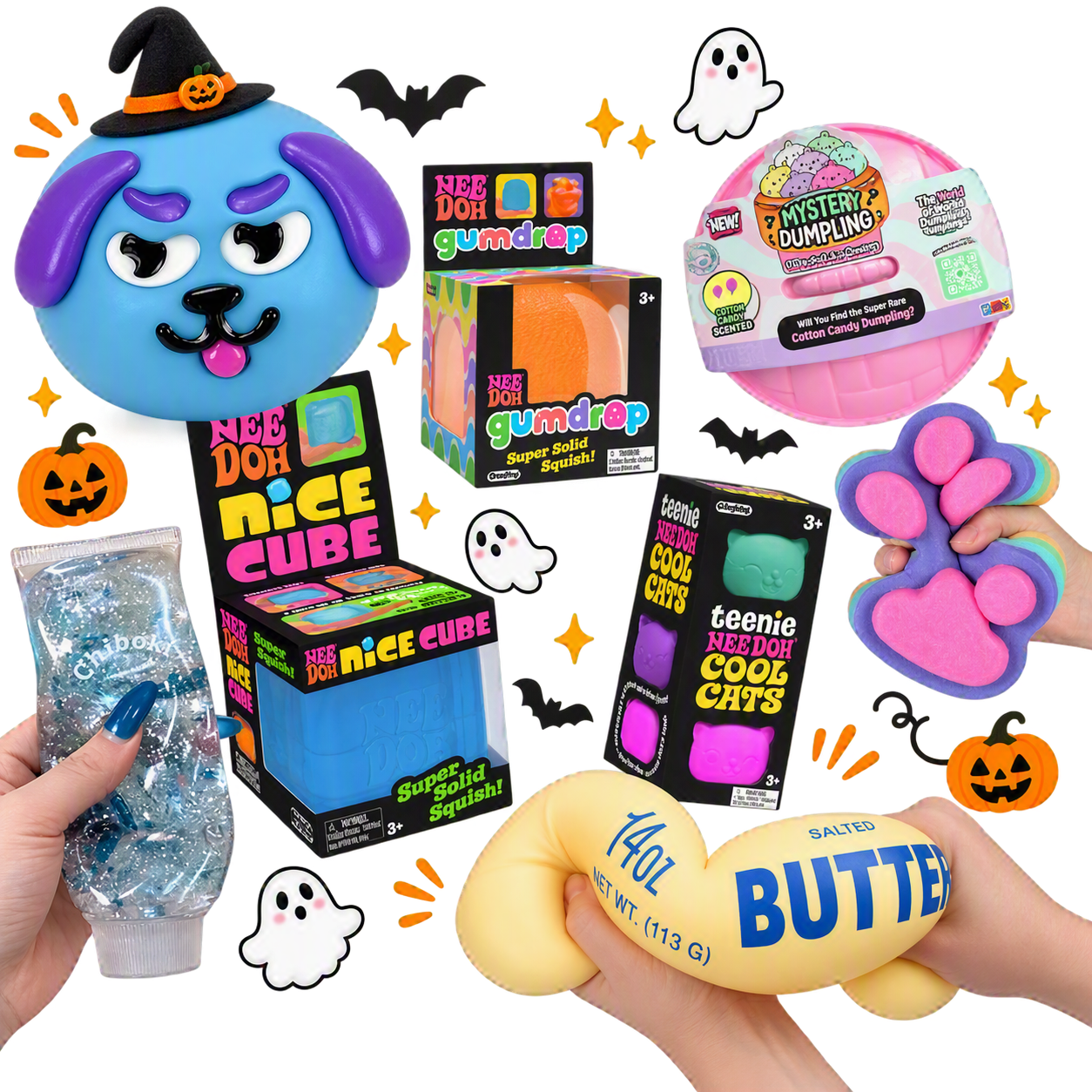 A collection of Halloween-themed toys and candies, including a blue dog-shaped squishy with purple ears wearing a witch hat, a pink cotton candy dumpling, a purple paw print squishy, an orange pumpkin bucket, a pack of glittery slime, a yellow butter squishy, and labeled boxes of toys like Nice Cube,' 'Gumdrop,' and 'Teenie Needoh Cool Cats'.