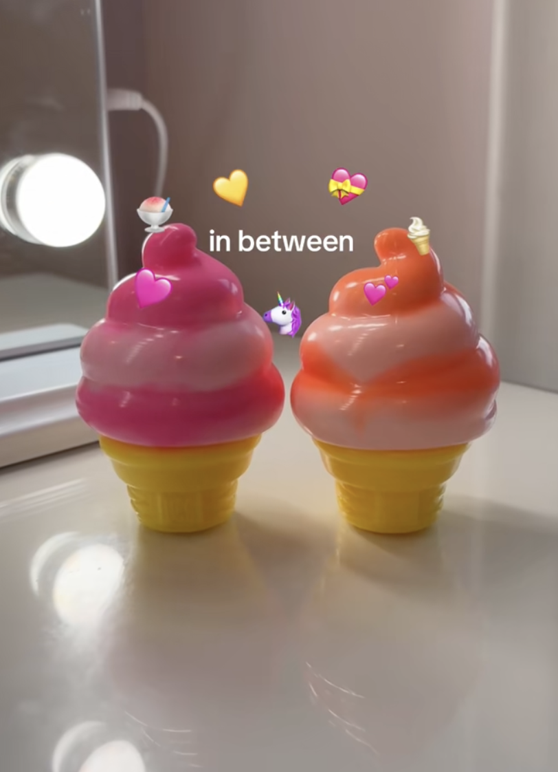 Two colorful ice cream cone-shaped candles with pink and orange swirled tops on a white surface, with emojis and text overlay saying "in between".